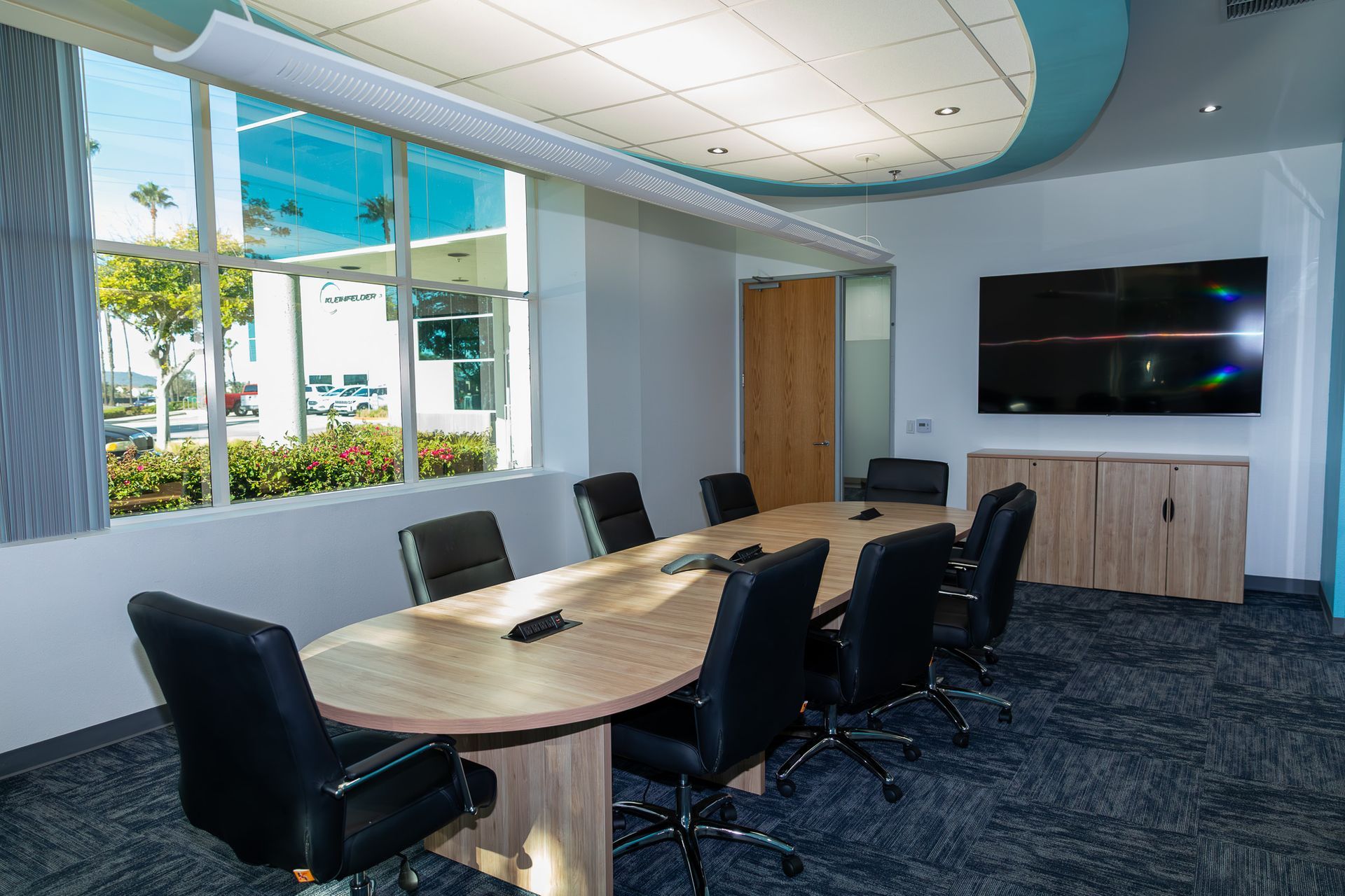 Conference room with oval table, black chairs, large window, and TV.