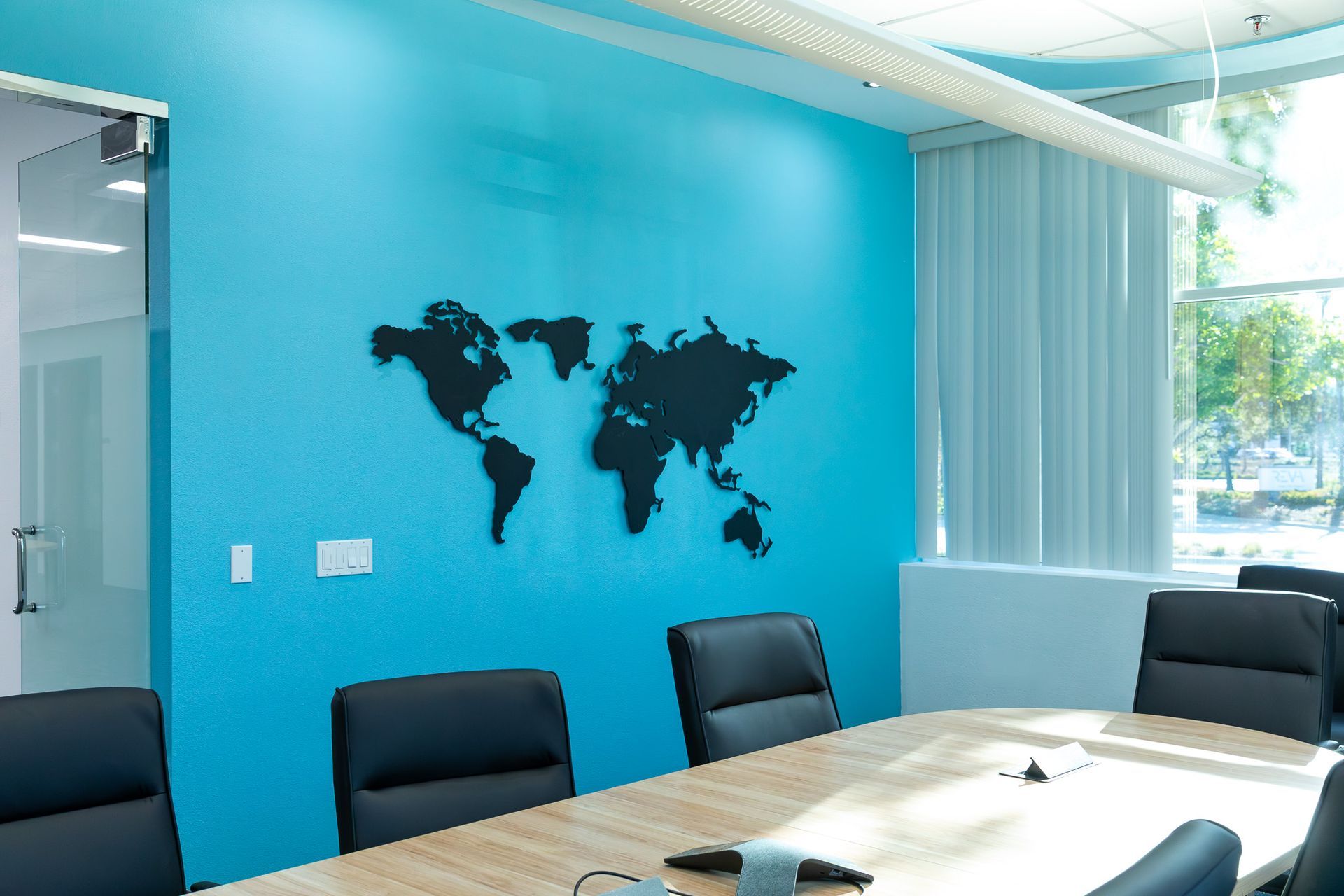 Conference room with blue wall, world map, and table with black chairs.