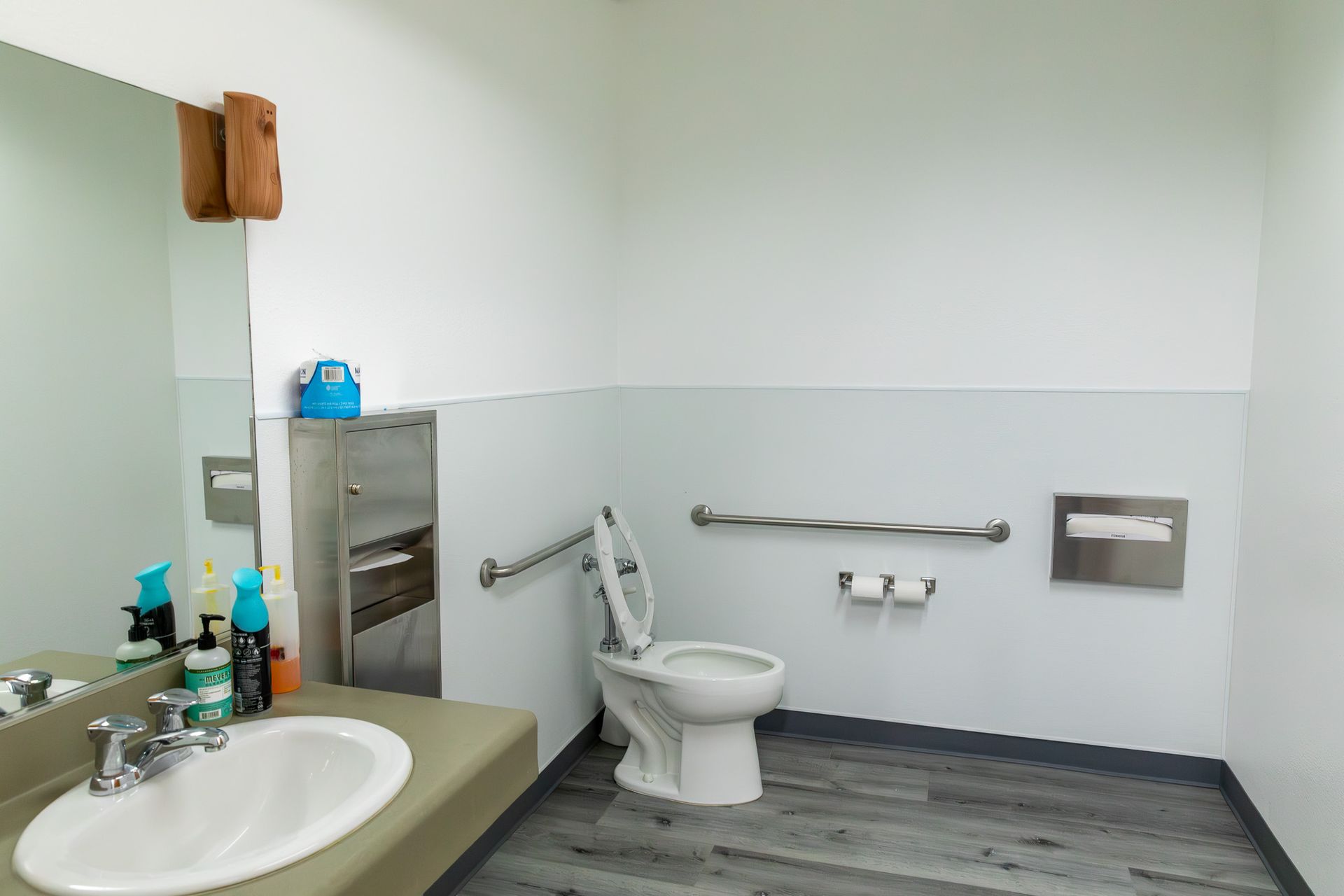 Accessible public restroom with toilet, sink, grab bar, and paper towel dispenser.