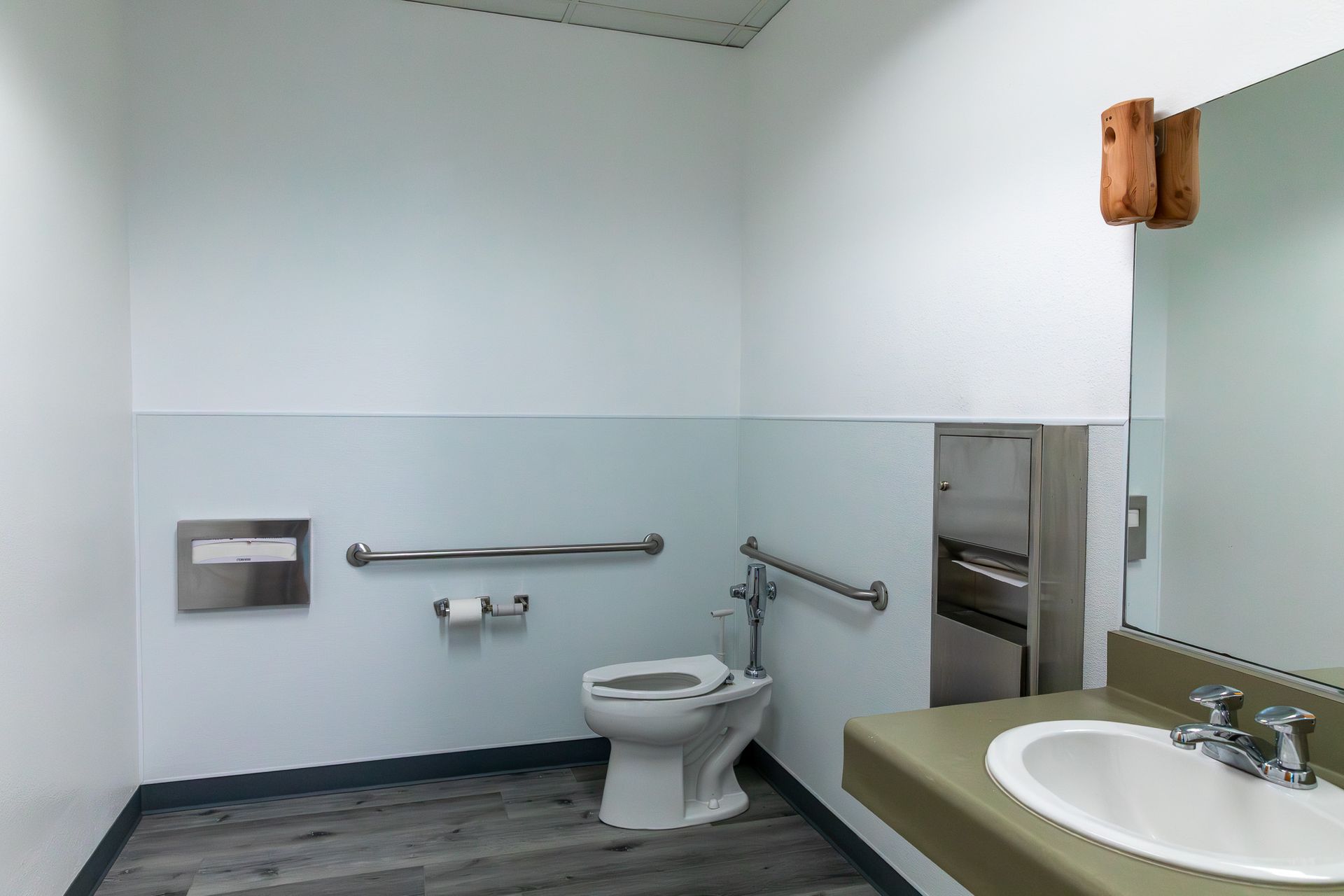 ADA-compliant public restroom with toilet, sink, and grab bars. Gray and white walls, neutral tones.