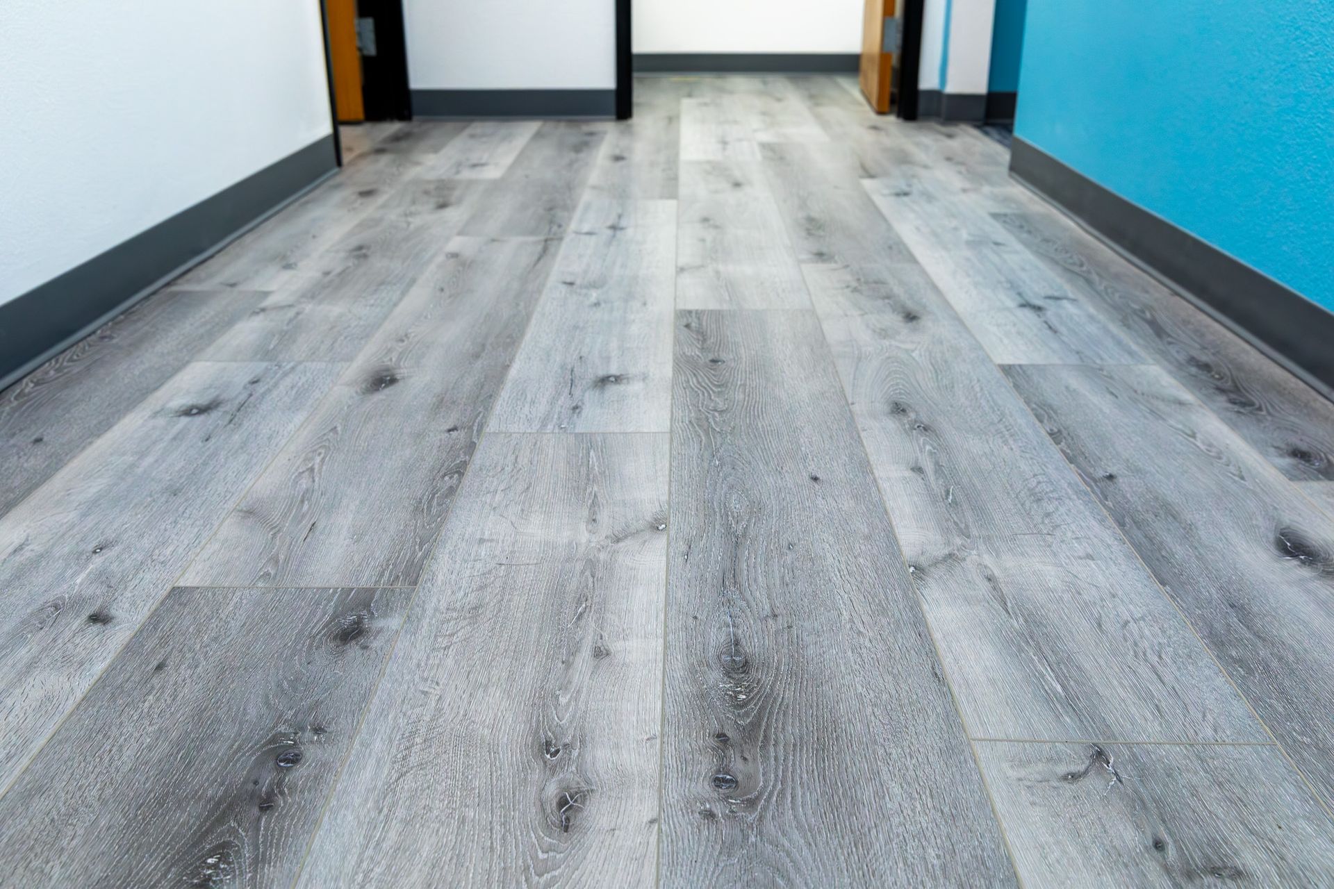 Gray wood-look flooring in a hallway with blue and white walls and dark doorways.
