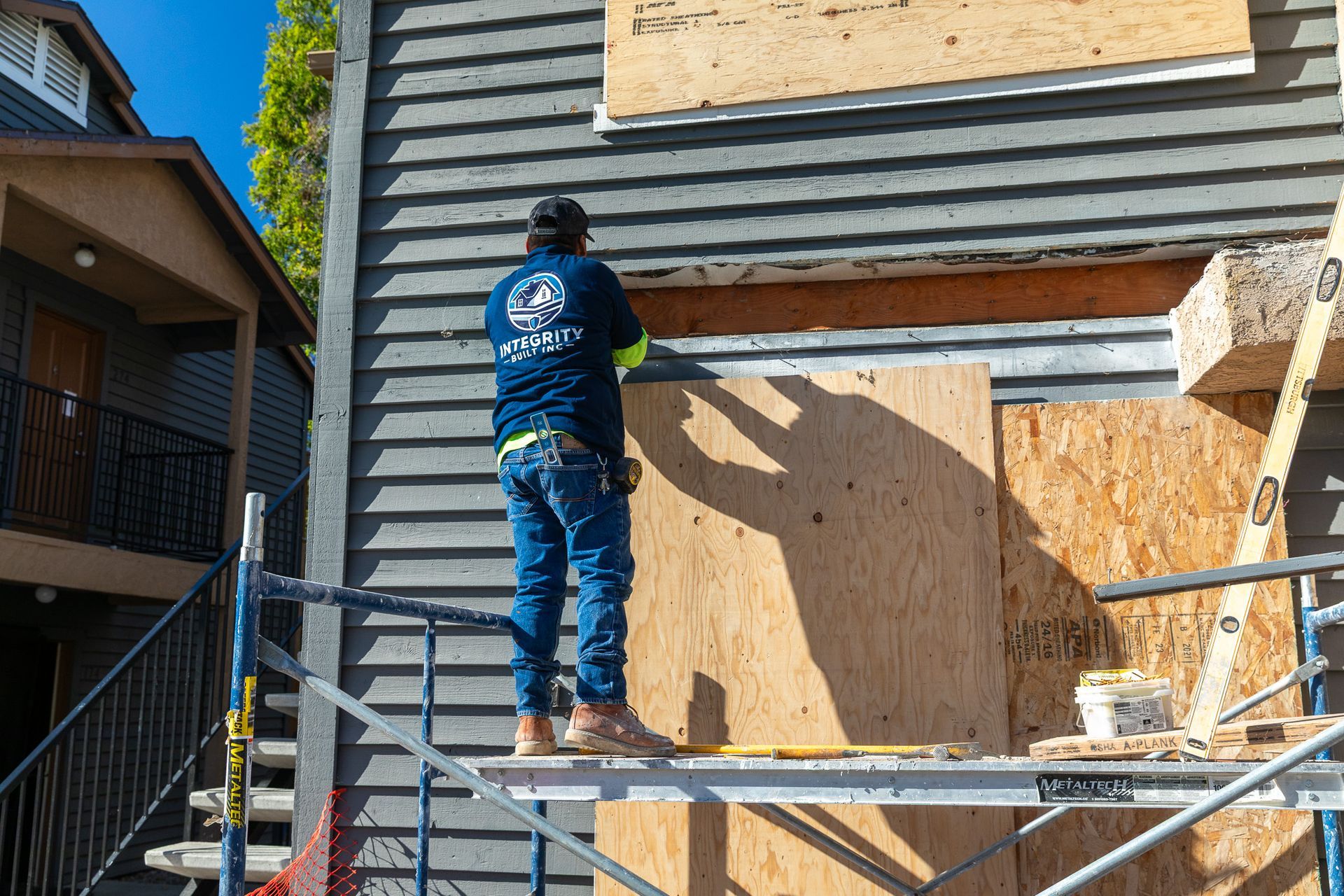 Construction worker on scaffolding boards up a house window with plywood.
