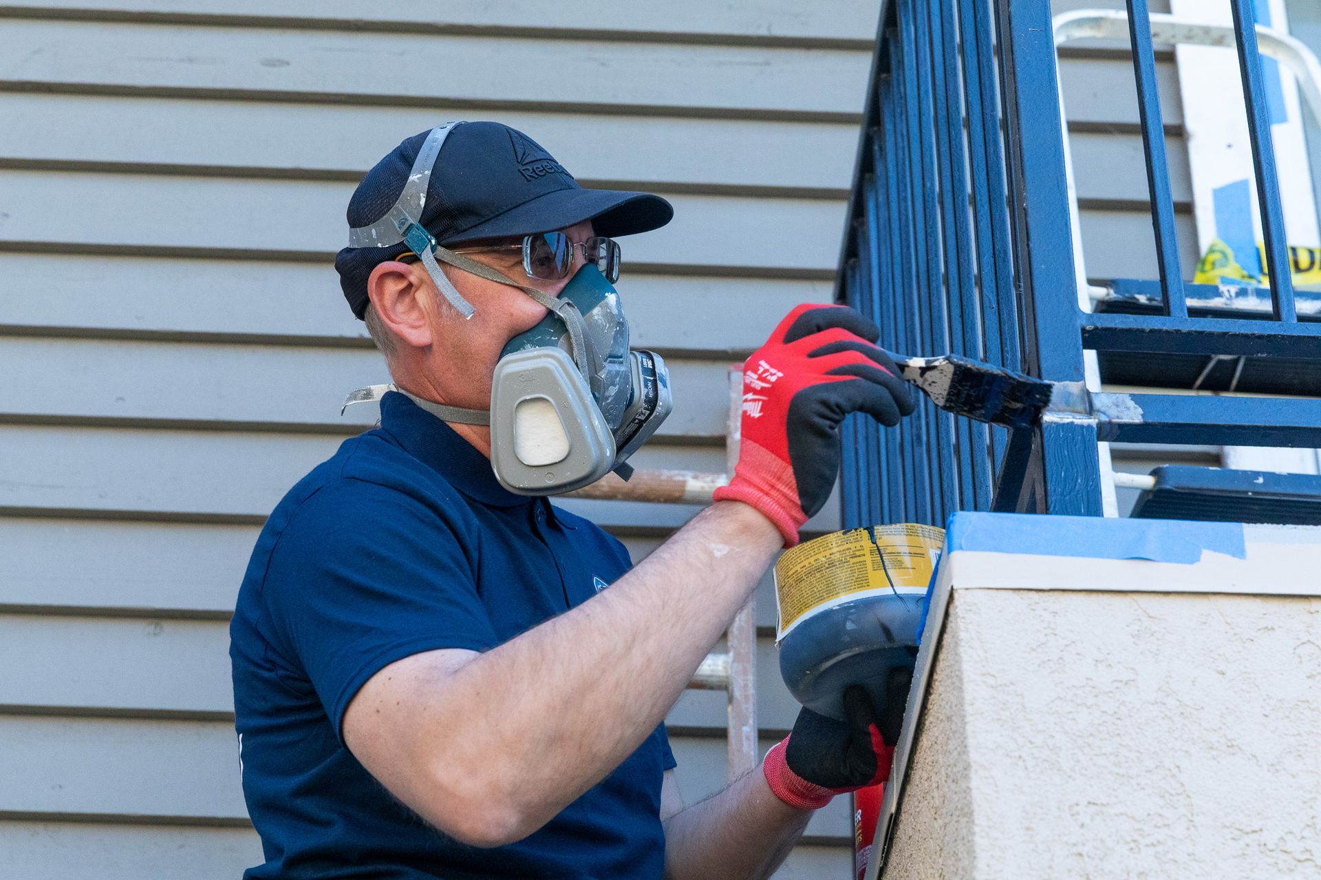 Person in respirator painting blue railing outdoors.
