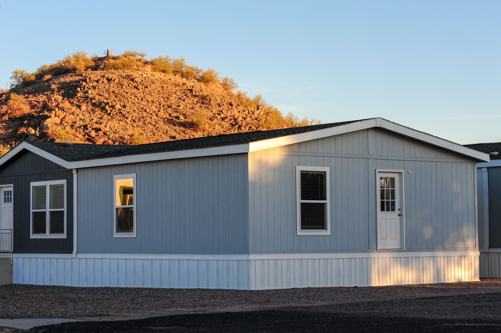Light blue mobile home with white trim and a mountain background.