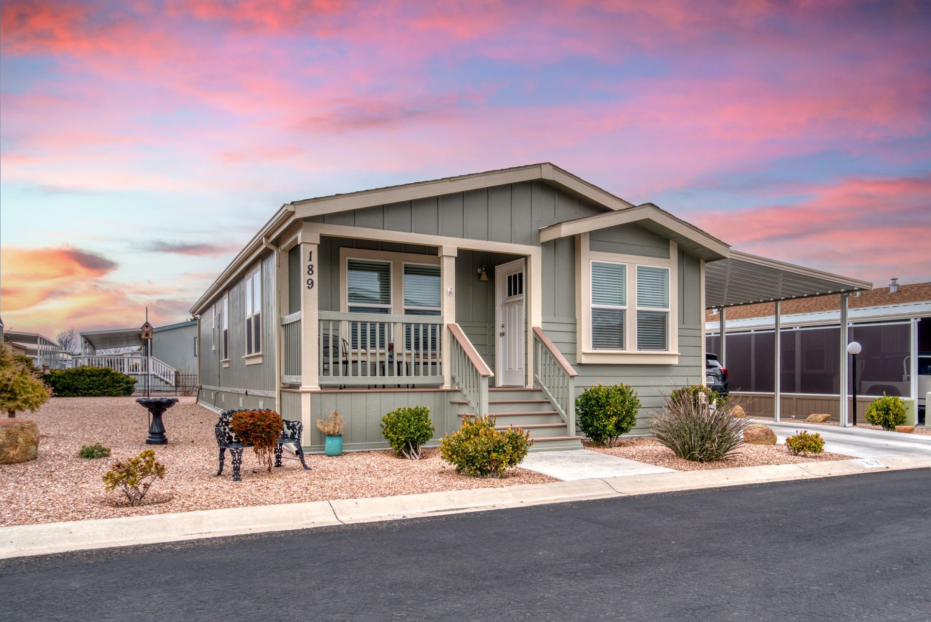Gray mobile home with porch, under a sunset sky.