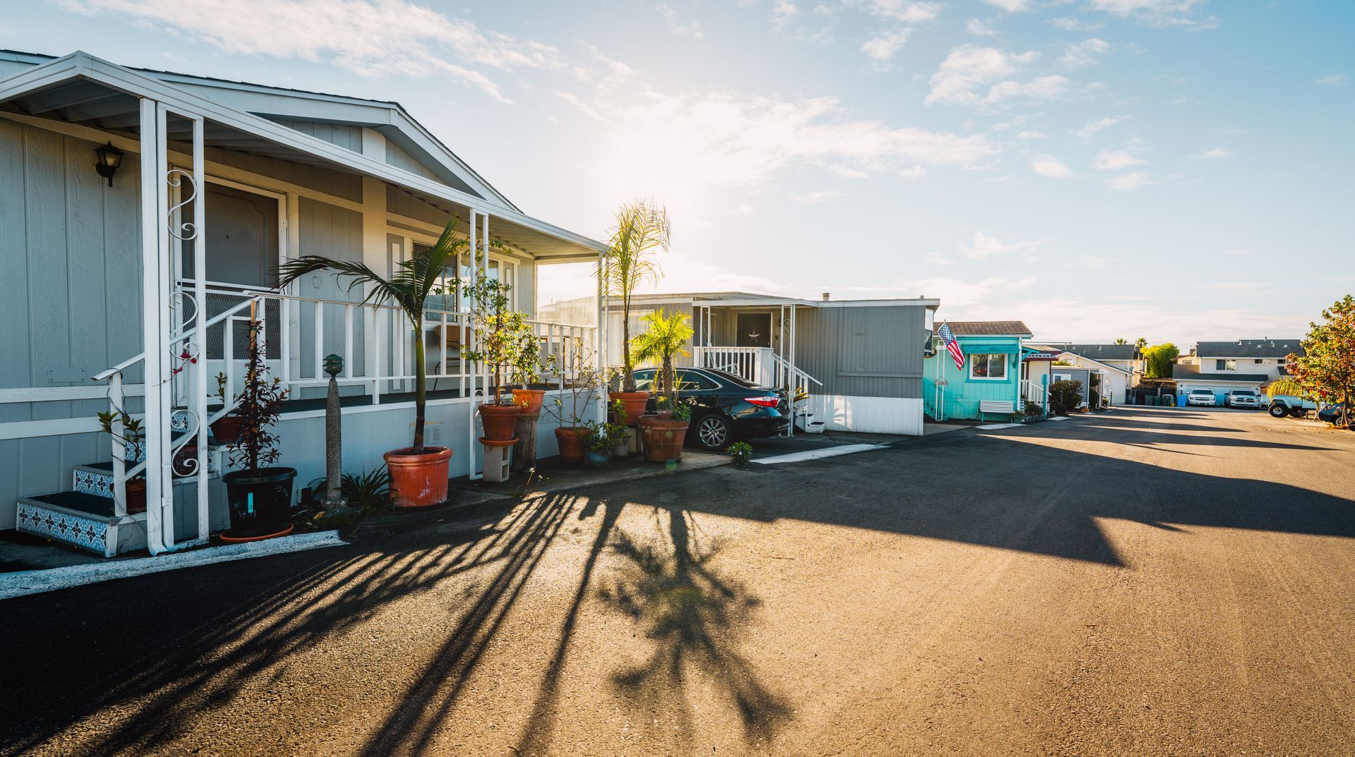 Mobile homes in a sunny neighborhood with parked cars and a clear sky.