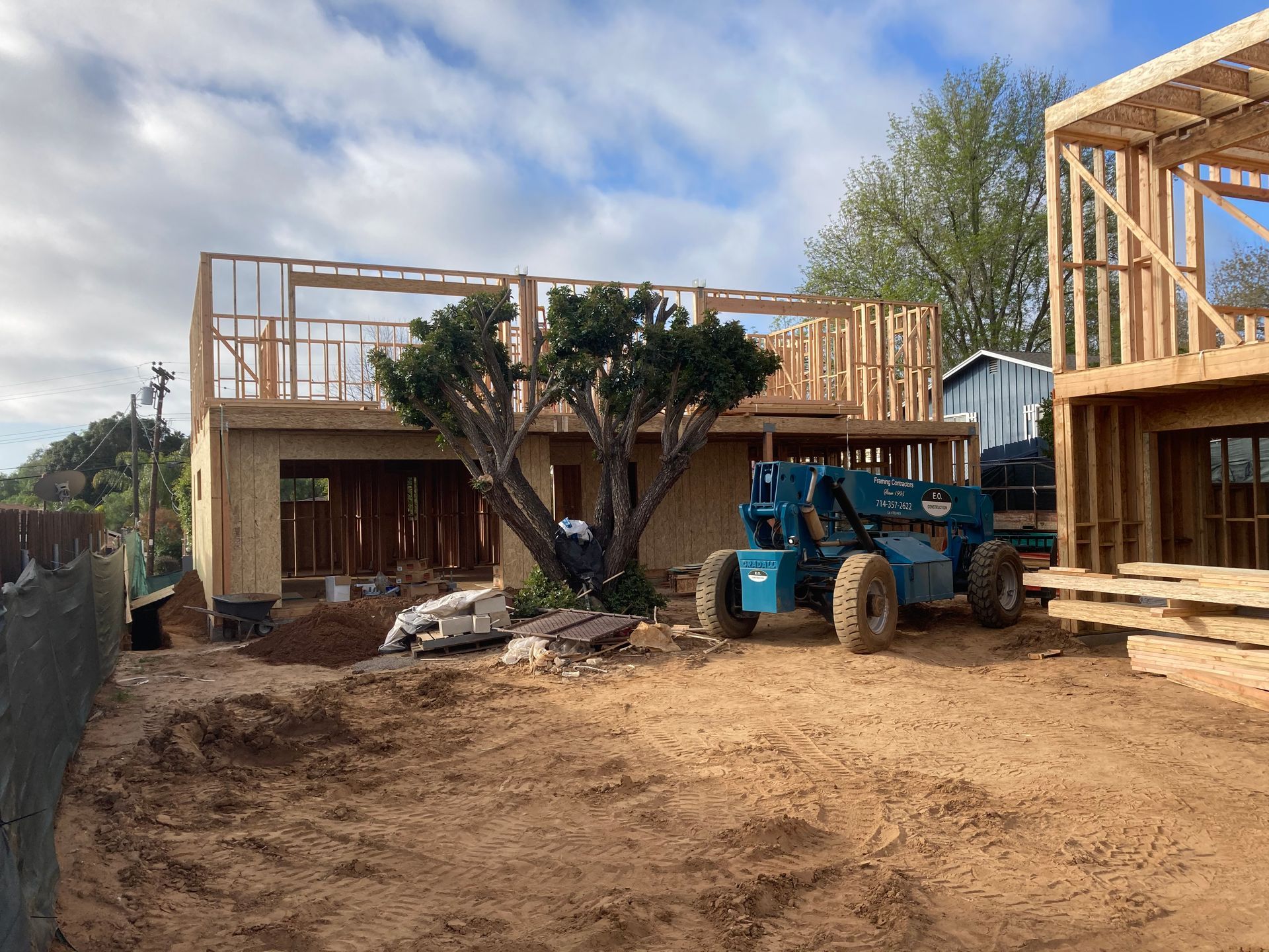 Construction site with two unfinished wooden houses and a blue telehandler machine.
