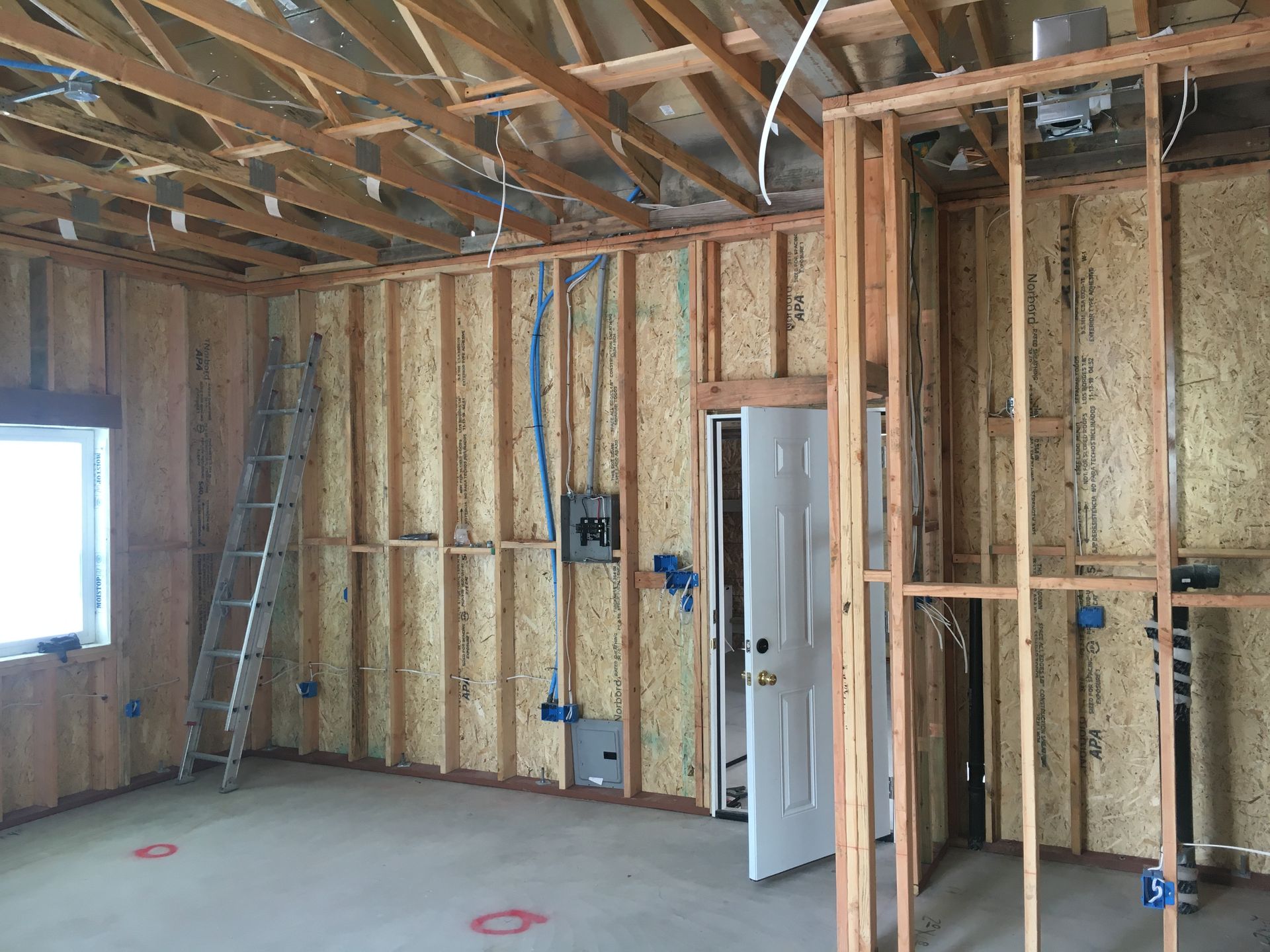 Interior view of a room under construction with exposed wooden framing and electrical wiring. A ladder is present.
