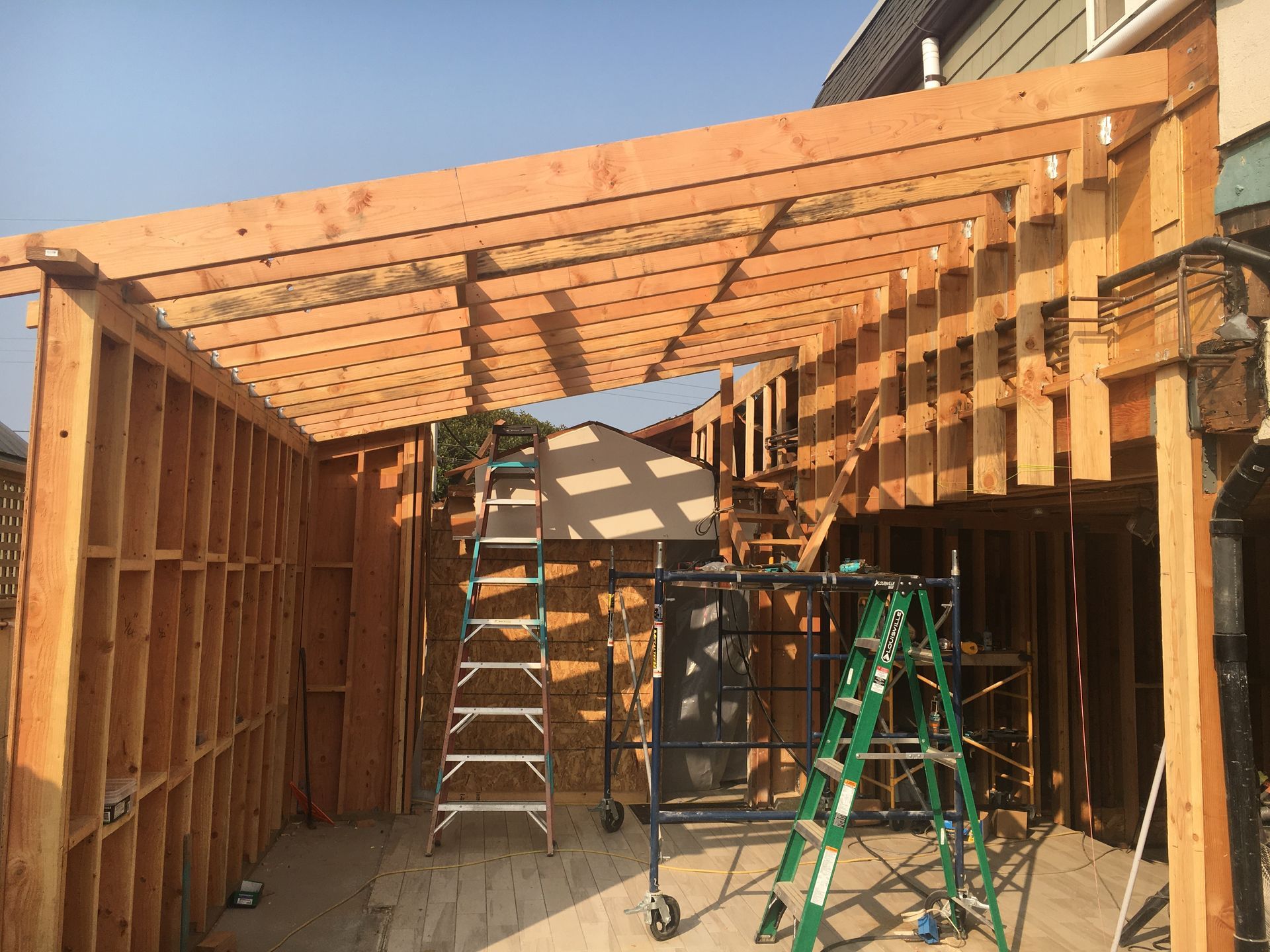 Wooden structure under construction, with ladders and tools inside; sunny outdoor setting.