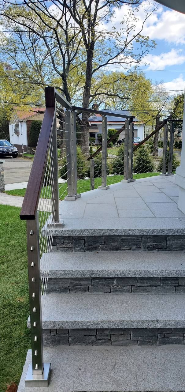 Staircase with metal railing leading to a house, surrounded by grass and trees.