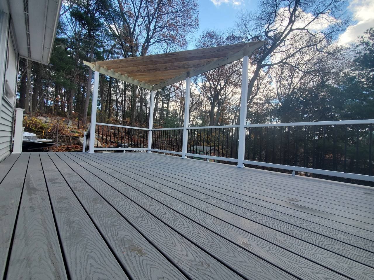 A gray composite deck with white railings and a canopy, surrounded by trees.