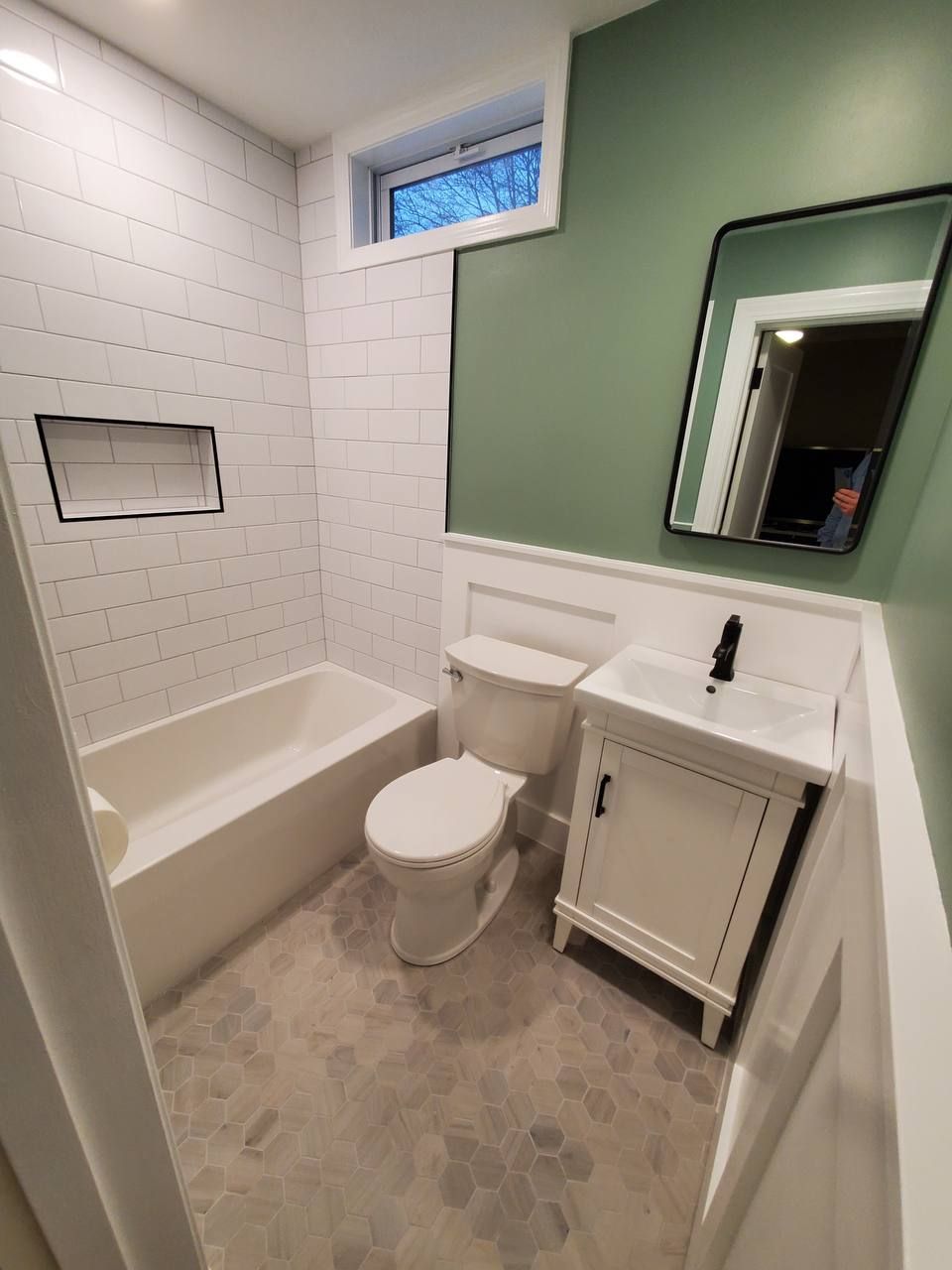 Newly renovated bathroom with white tile, green wall, white vanity, and tub.