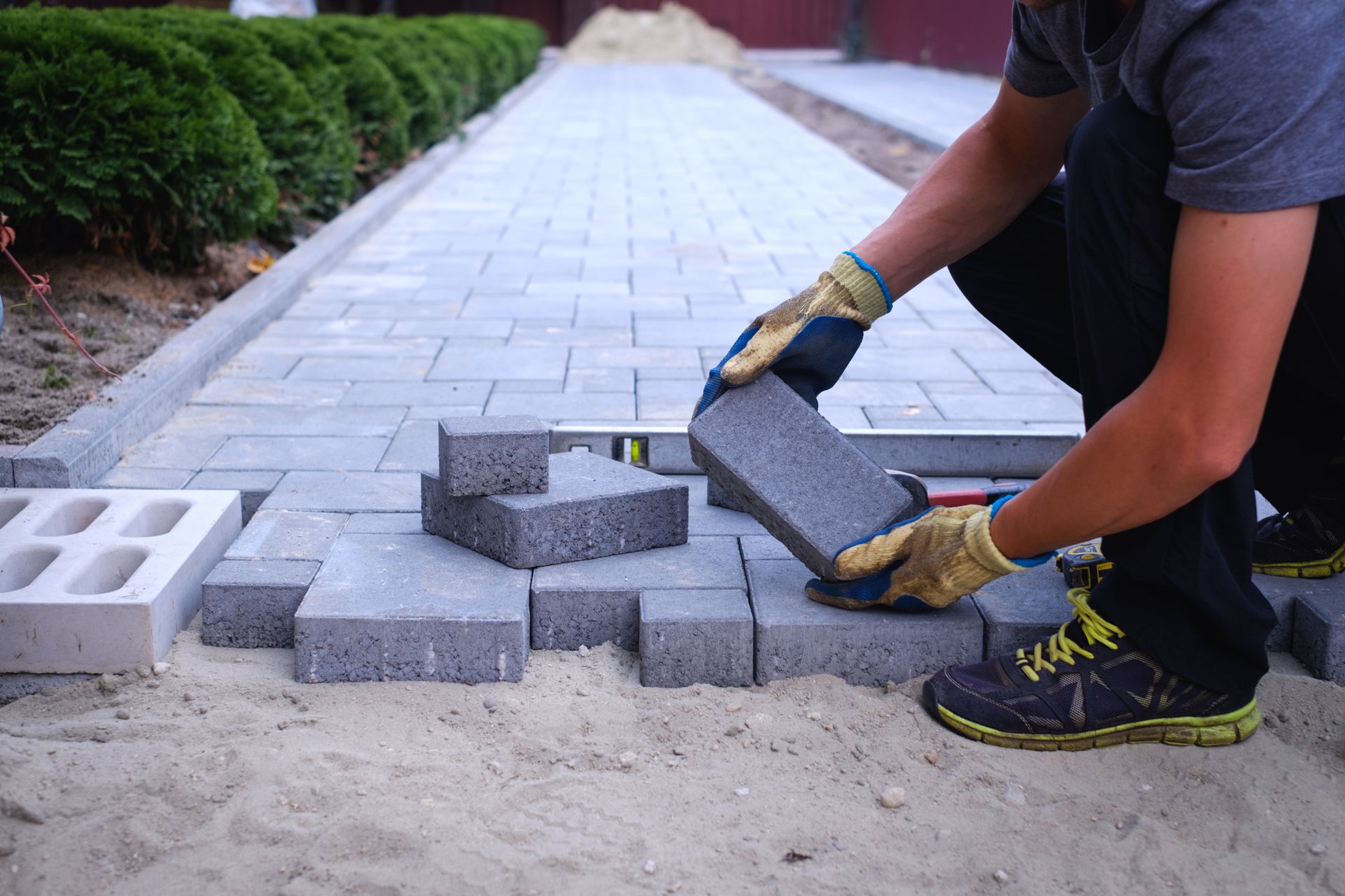 Worker placing concrete pavers on a sand base to build a patterned walkway with straight edges and l