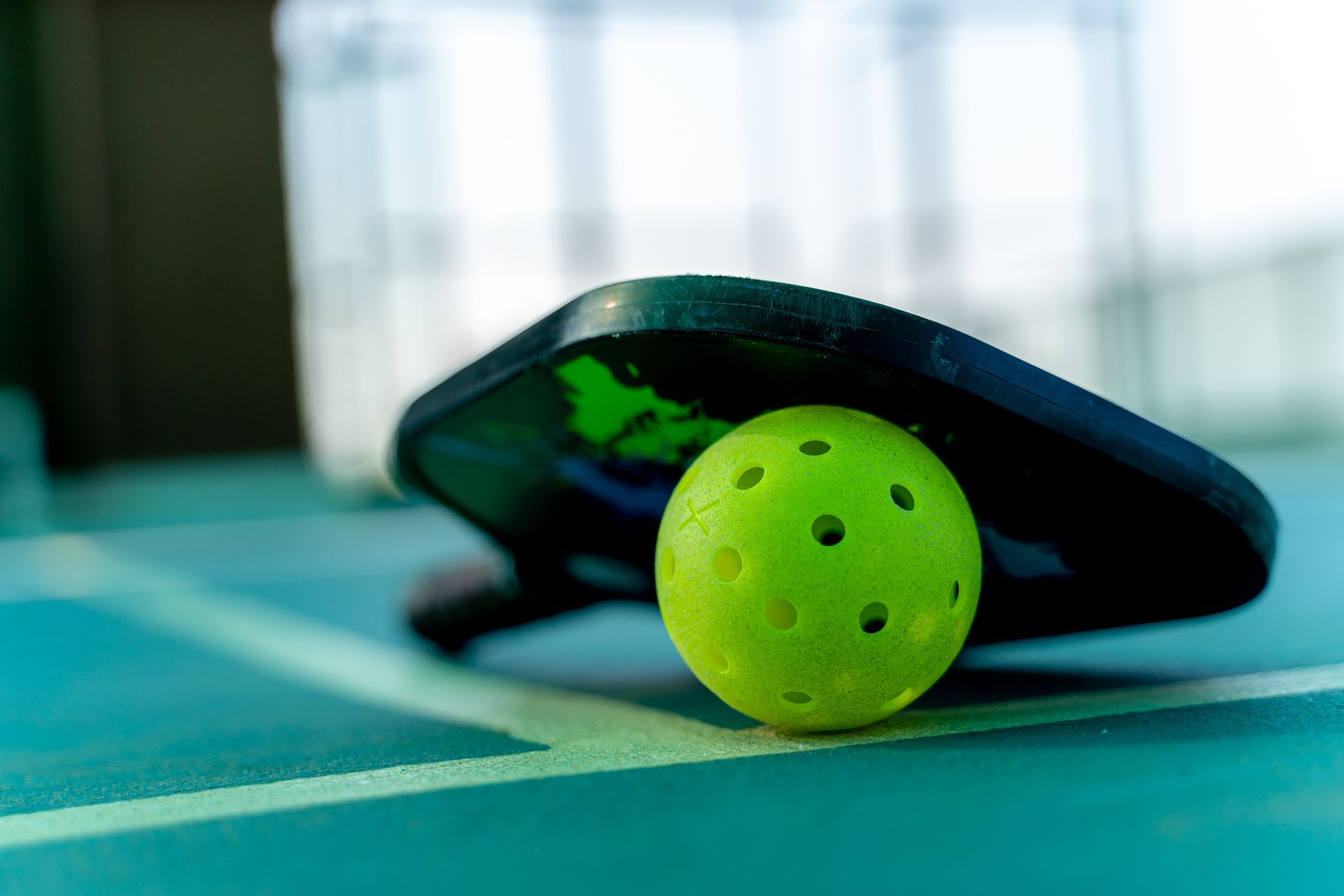 A yellow ball is sitting on top of a paddle on a tennis court.