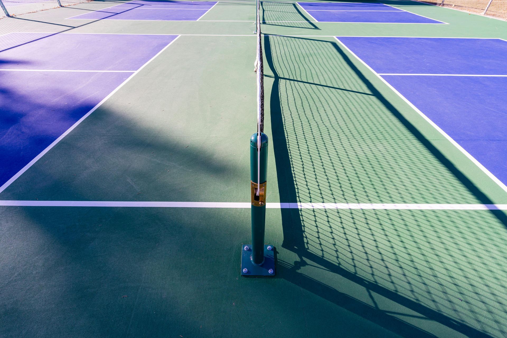 An empty tennis court in a park with trees in the background.