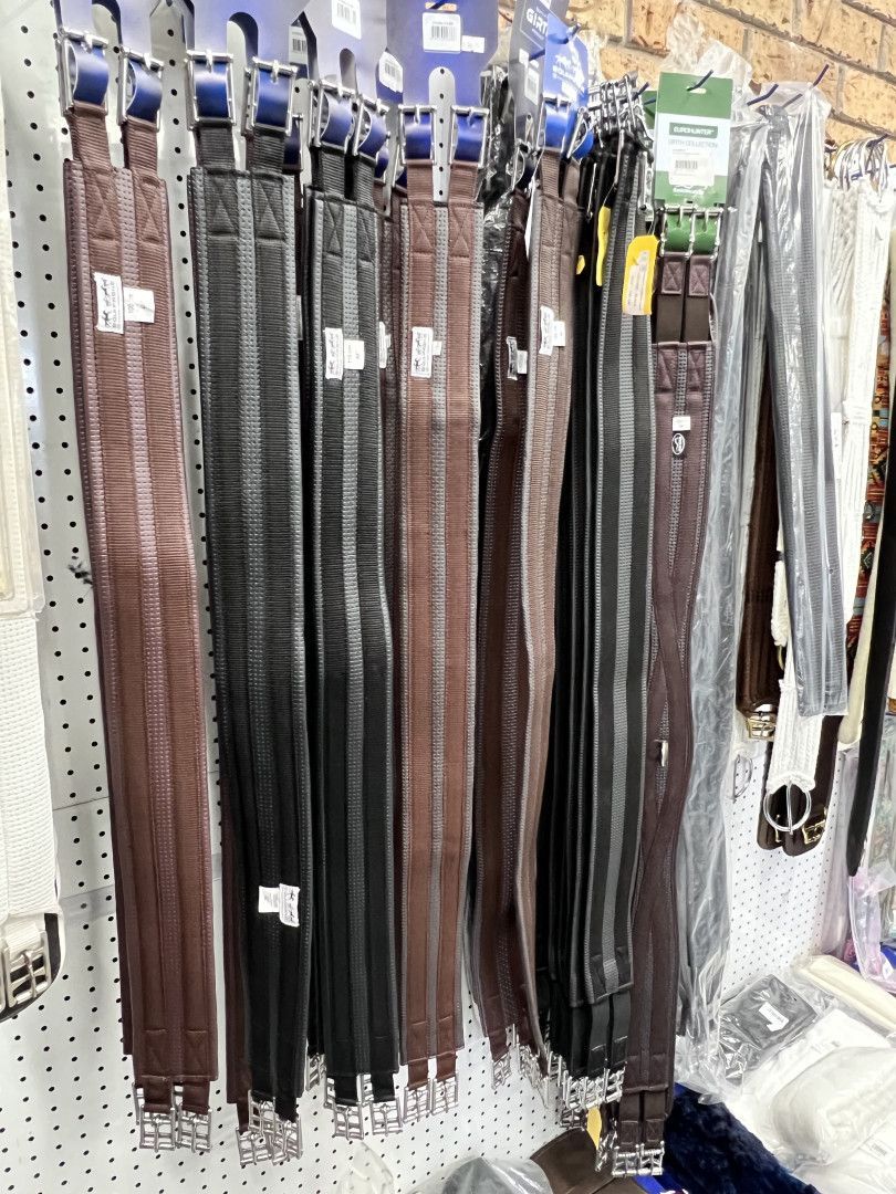 Rows of equestrian girths in various colors, hanging on display. - — Paint Horse Saddlery In Taree, NSW