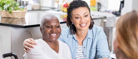 A woman is sitting next to an older woman in a wheelchair.