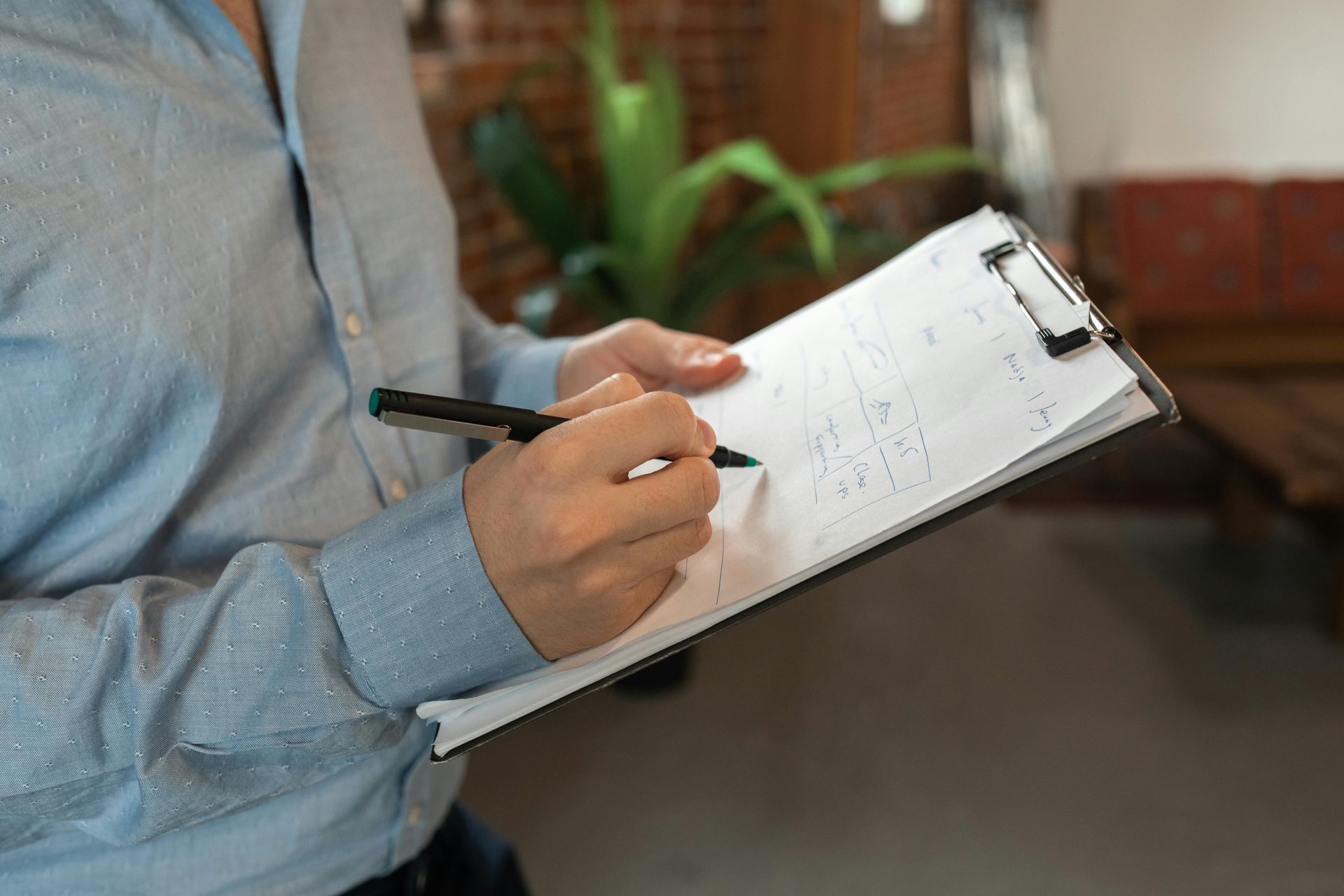 Person writing on a clipboard with a pen indoors, wearing a light blue shirt.