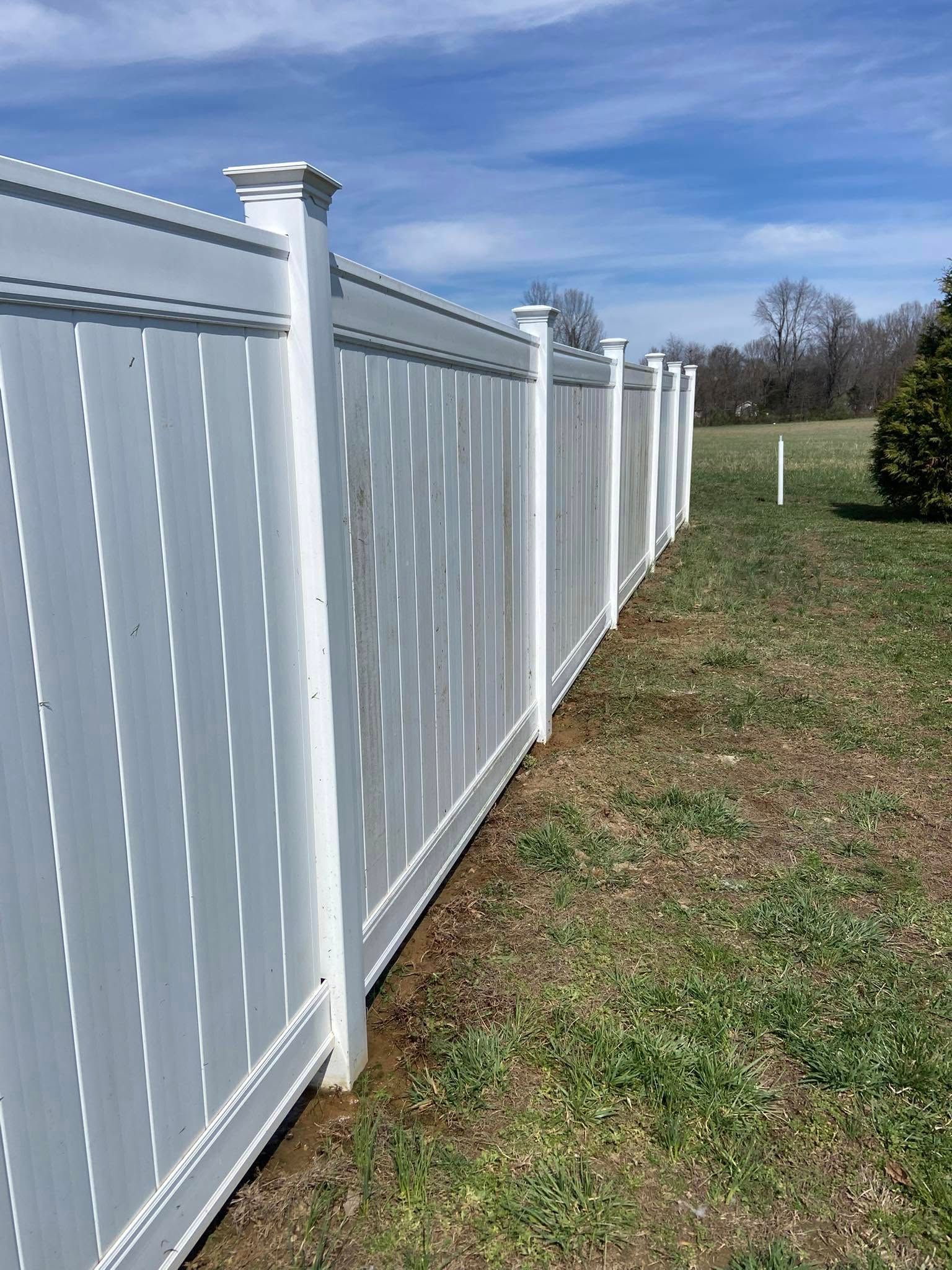 White vinyl fence in a grassy yard under a blue sky.