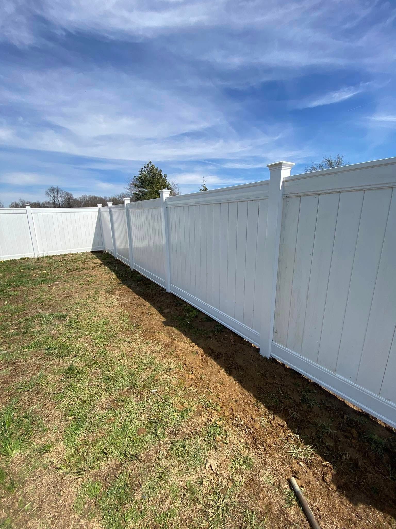 White vinyl fence in a grassy yard under a blue sky.