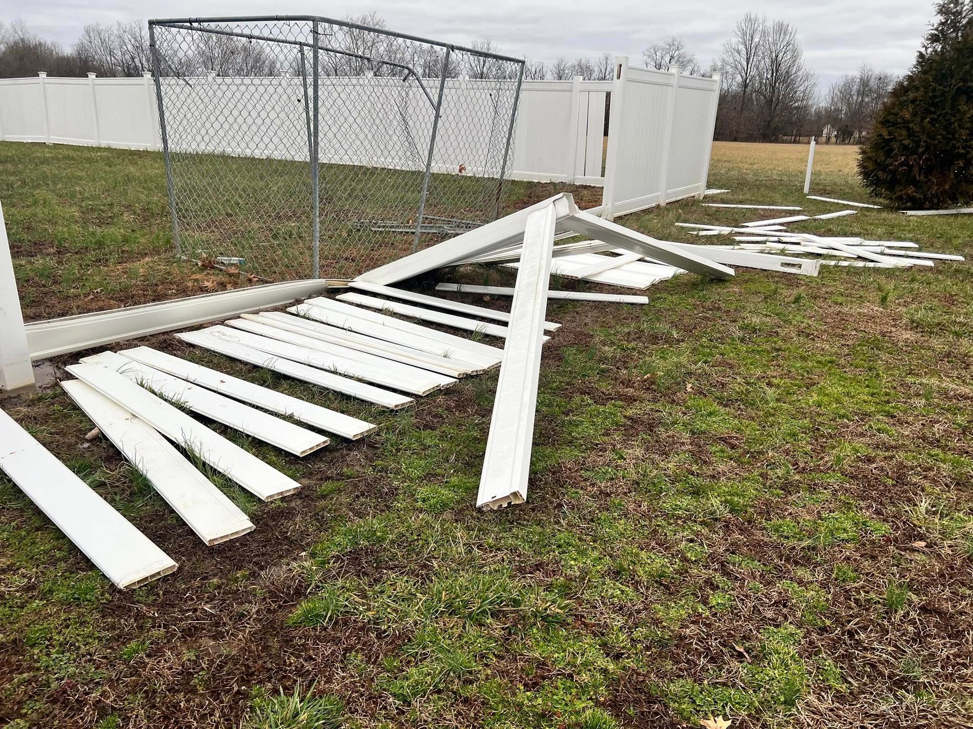 A fallen white fence with scattered boards on a grassy yard, near a chain-link fence and white privacy fence.