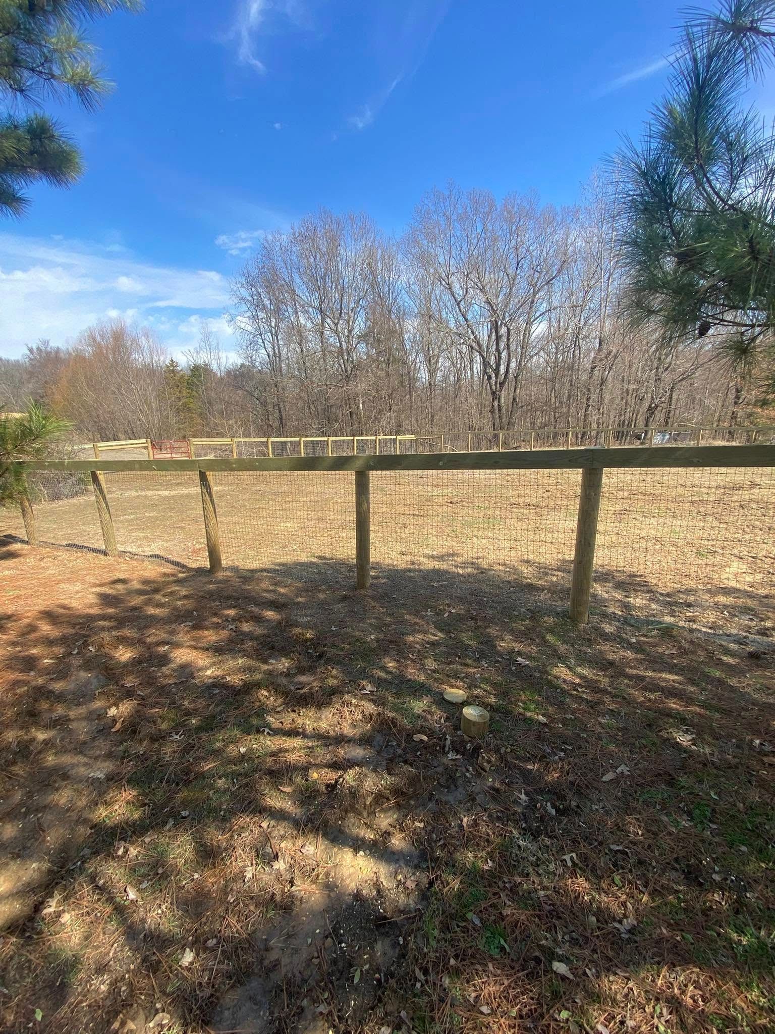 A wooden fence in a grassy area, trees and blue sky background.