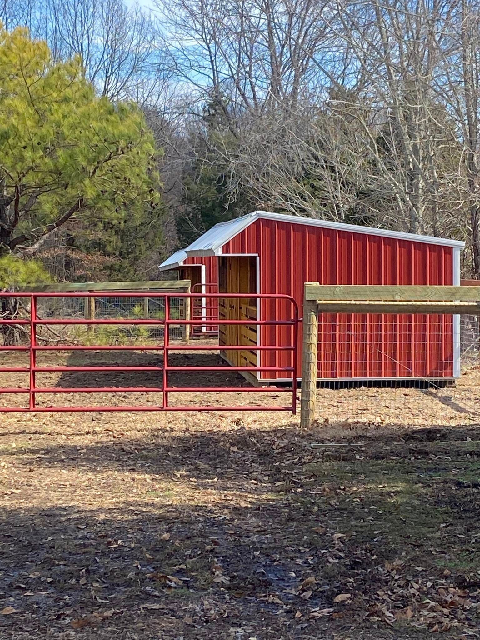 Red shed with white trim behind a red metal fence in a wooded area.