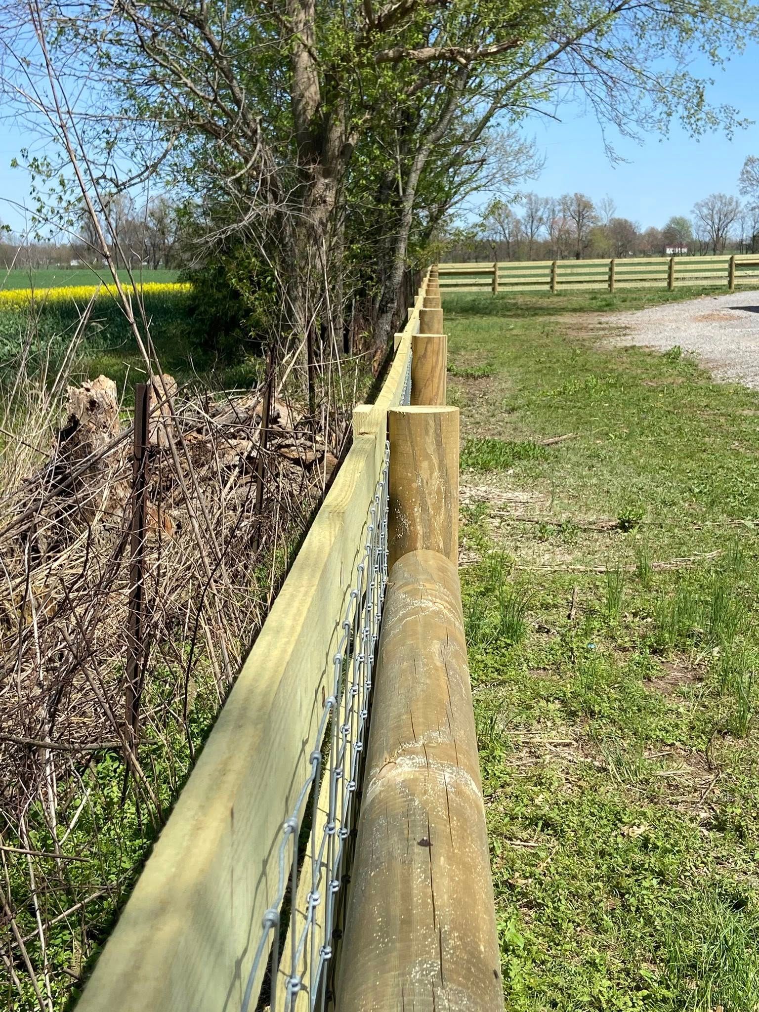 Wooden fence with wire mesh in a grassy field, near trees.
