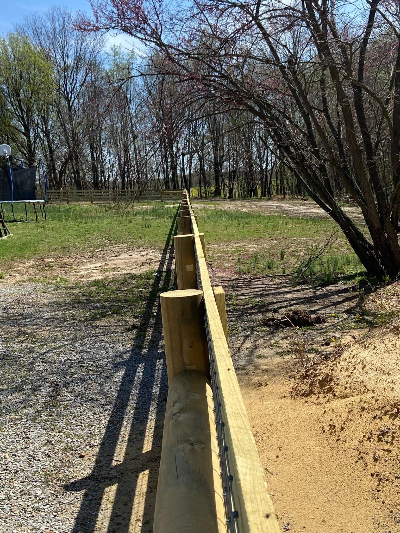 Wooden fence posts and rail with a gravel path and grassy field.