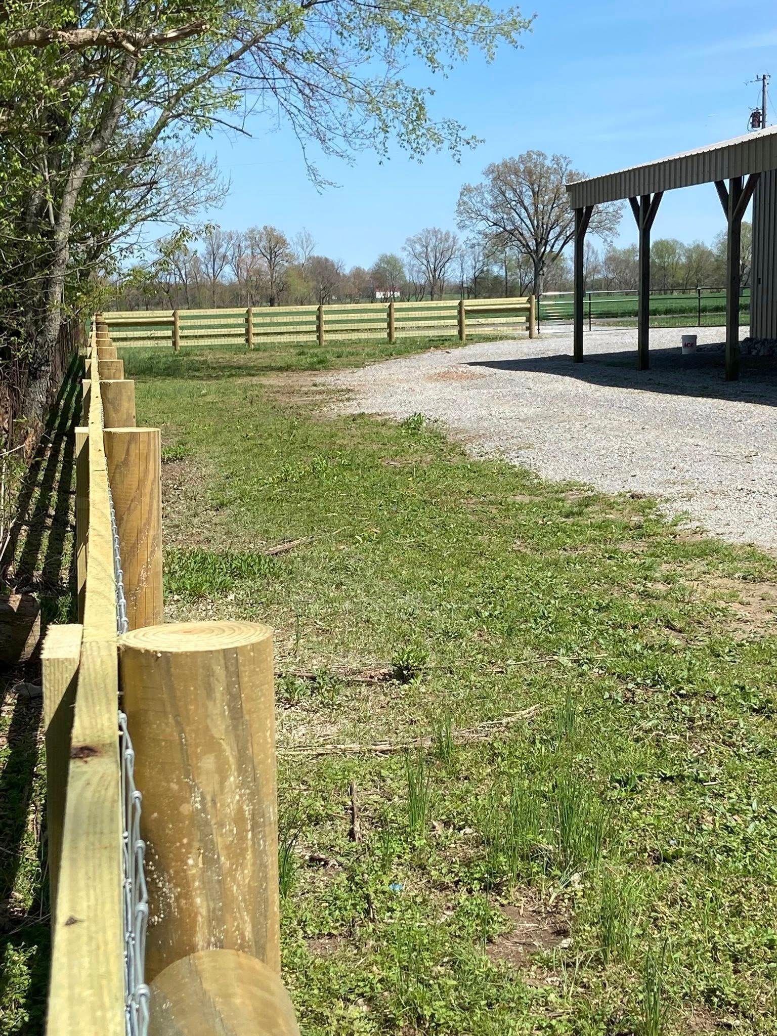 Wooden fence along a grassy area, gravel path next to a barn on a sunny day.