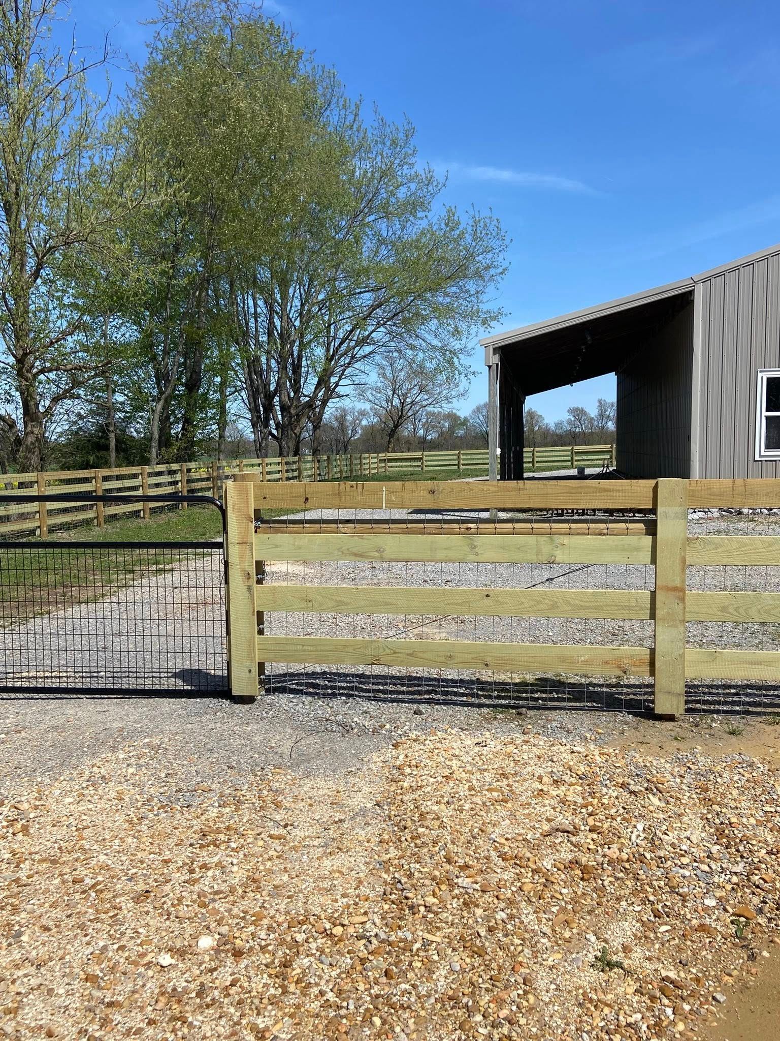 Wooden fence with gravel driveway and gray barn on sunny day.