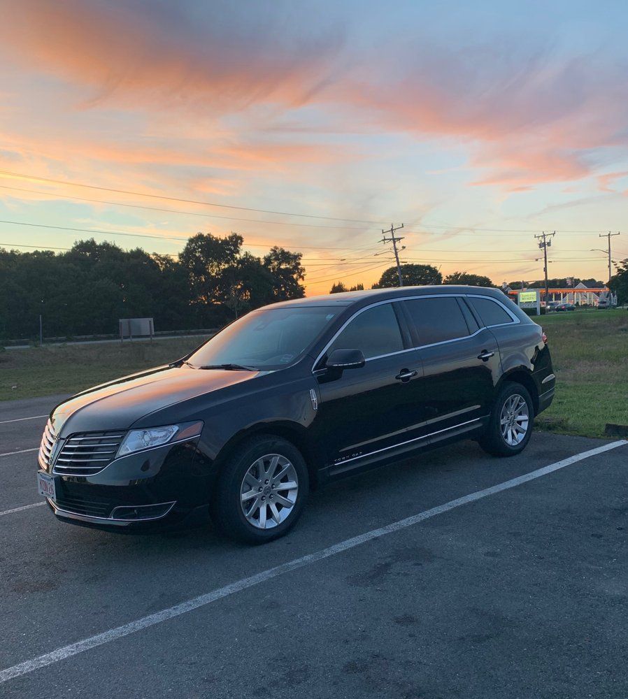 A black car is parked in a parking lot at sunset.