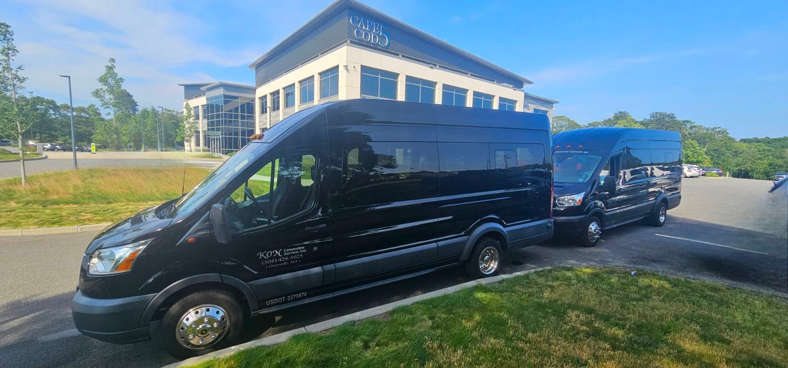 Two black vans are parked in a parking lot in front of a building.