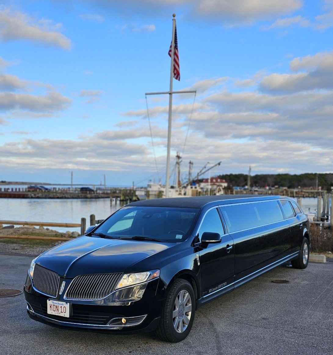 A black limousine is parked in front of a body of water.