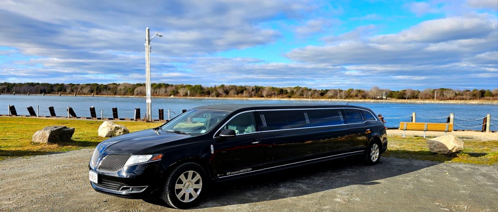A black limousine is parked in front of a body of water.