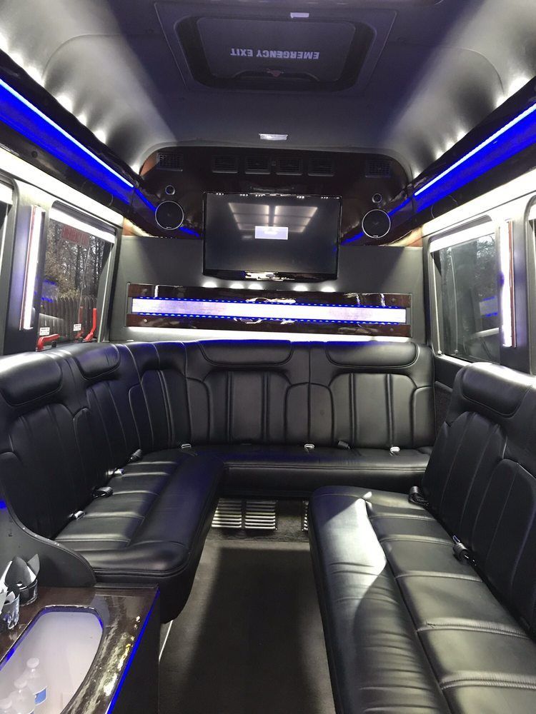The inside of a limousine with black leather seats and a flat screen tv.