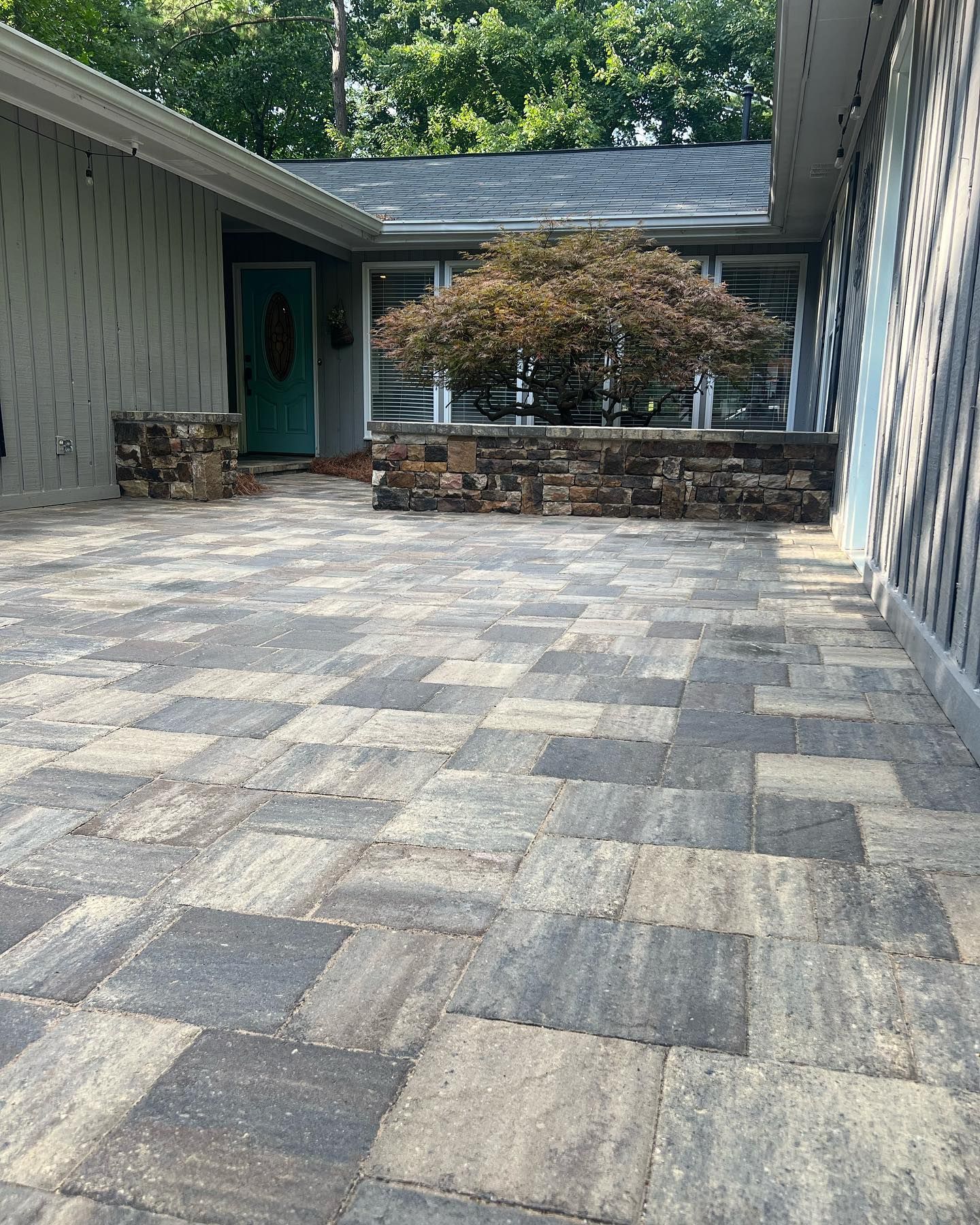 Stone patio entrance with a tree and teal door.