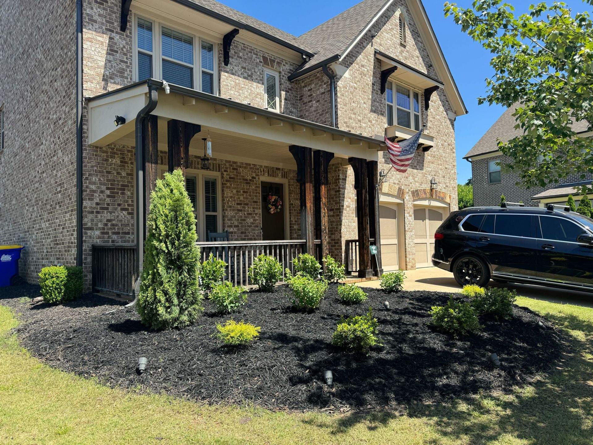 Brick house with black mulch landscaping, a porch, and a black SUV parked.