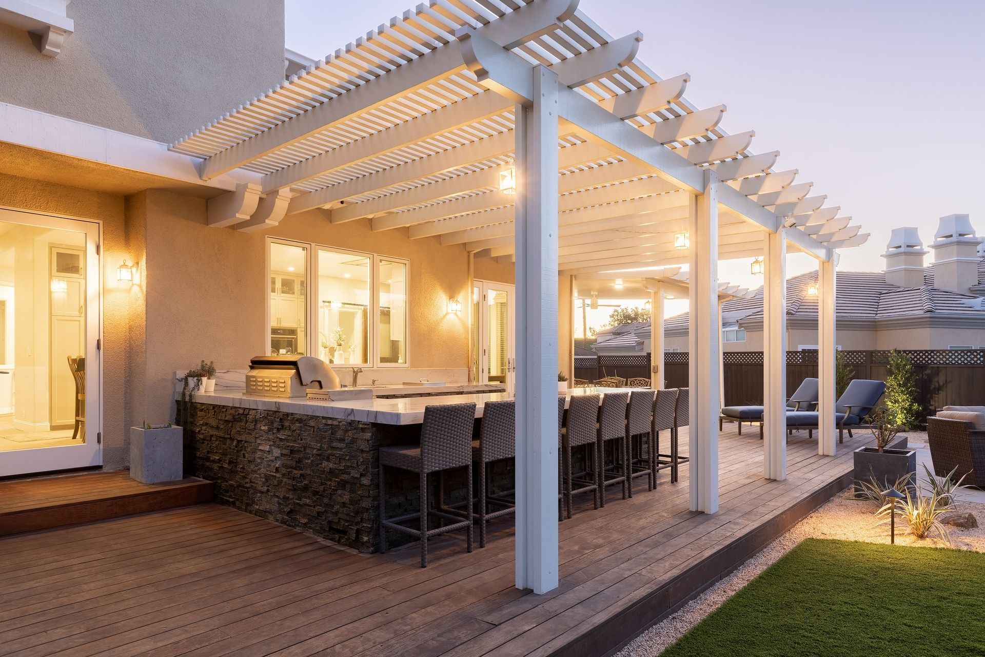 Outdoor patio with white pergola, bar seating, and glowing lights.