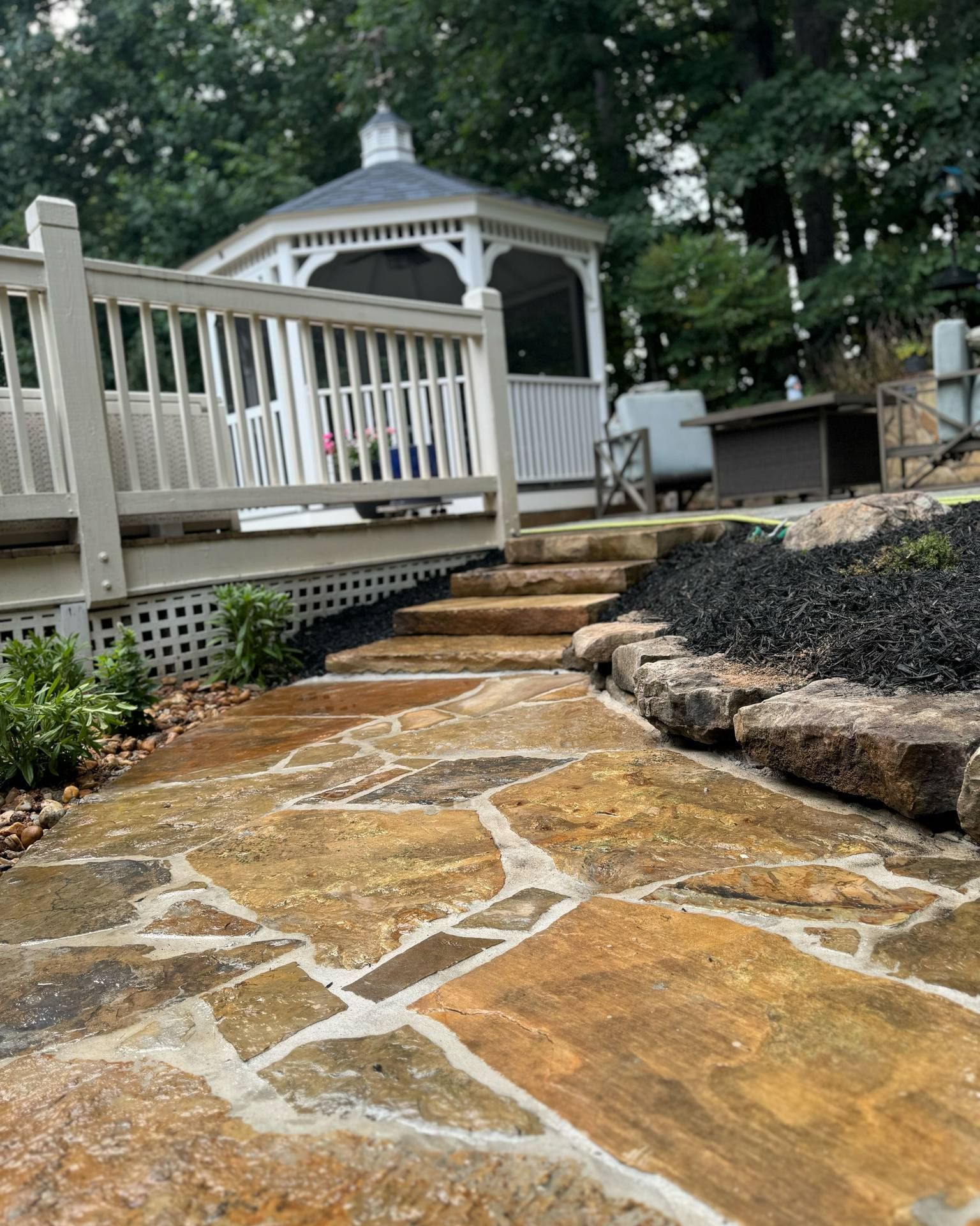 Stone pathway leading to a gazebo and deck, lined with rocks and black mulch.