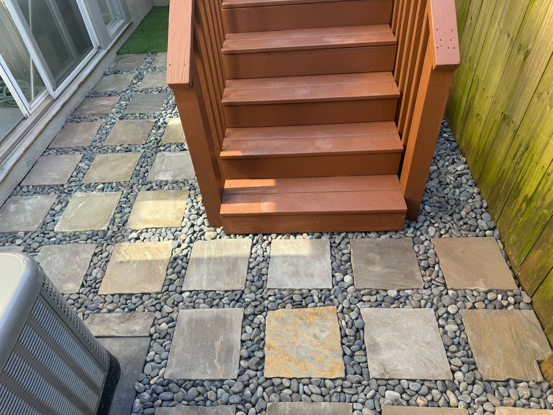 Stone pavers and gravel pathway beneath wooden stairs.