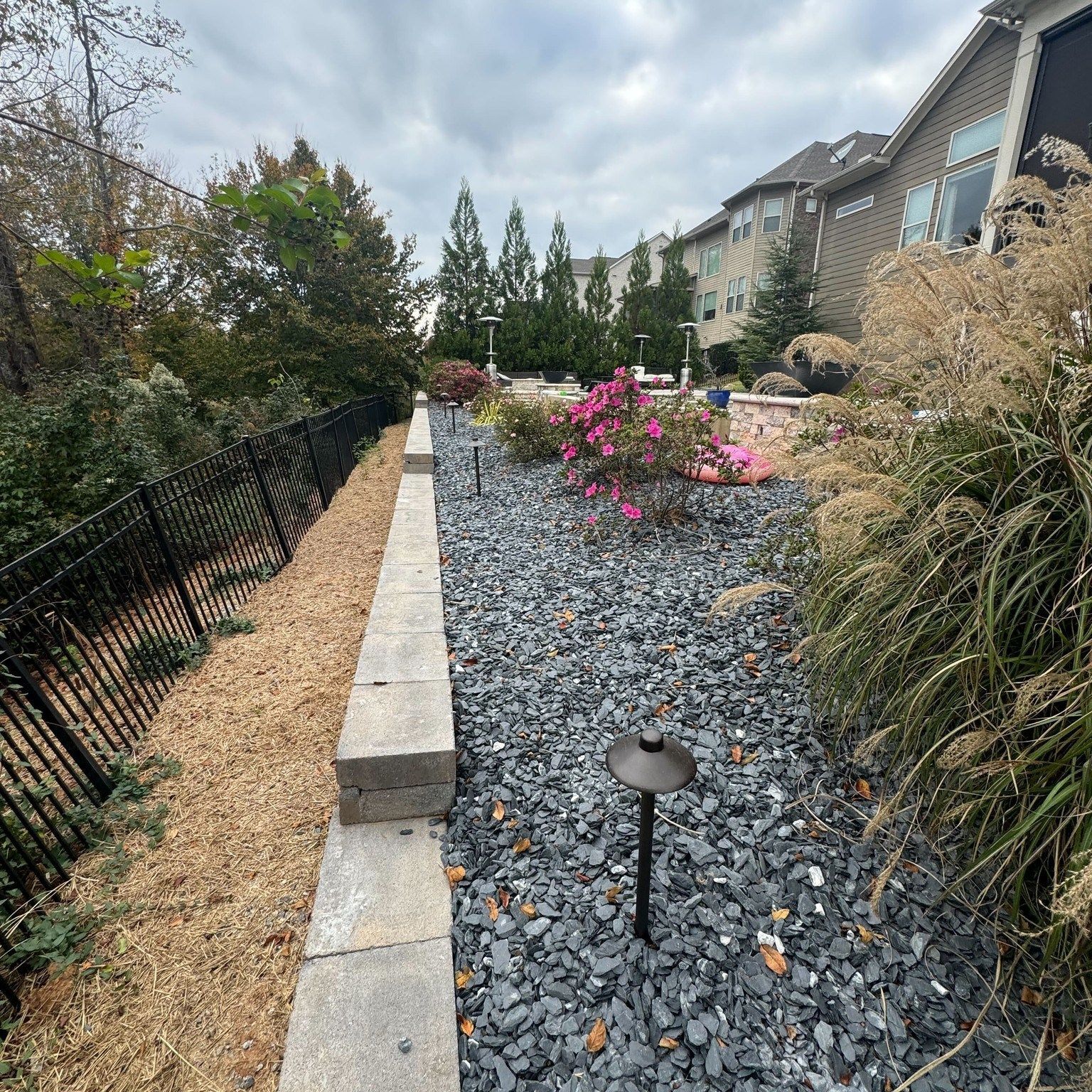 A landscaped backyard with a stone wall, dark gravel, bushes, and path lights.