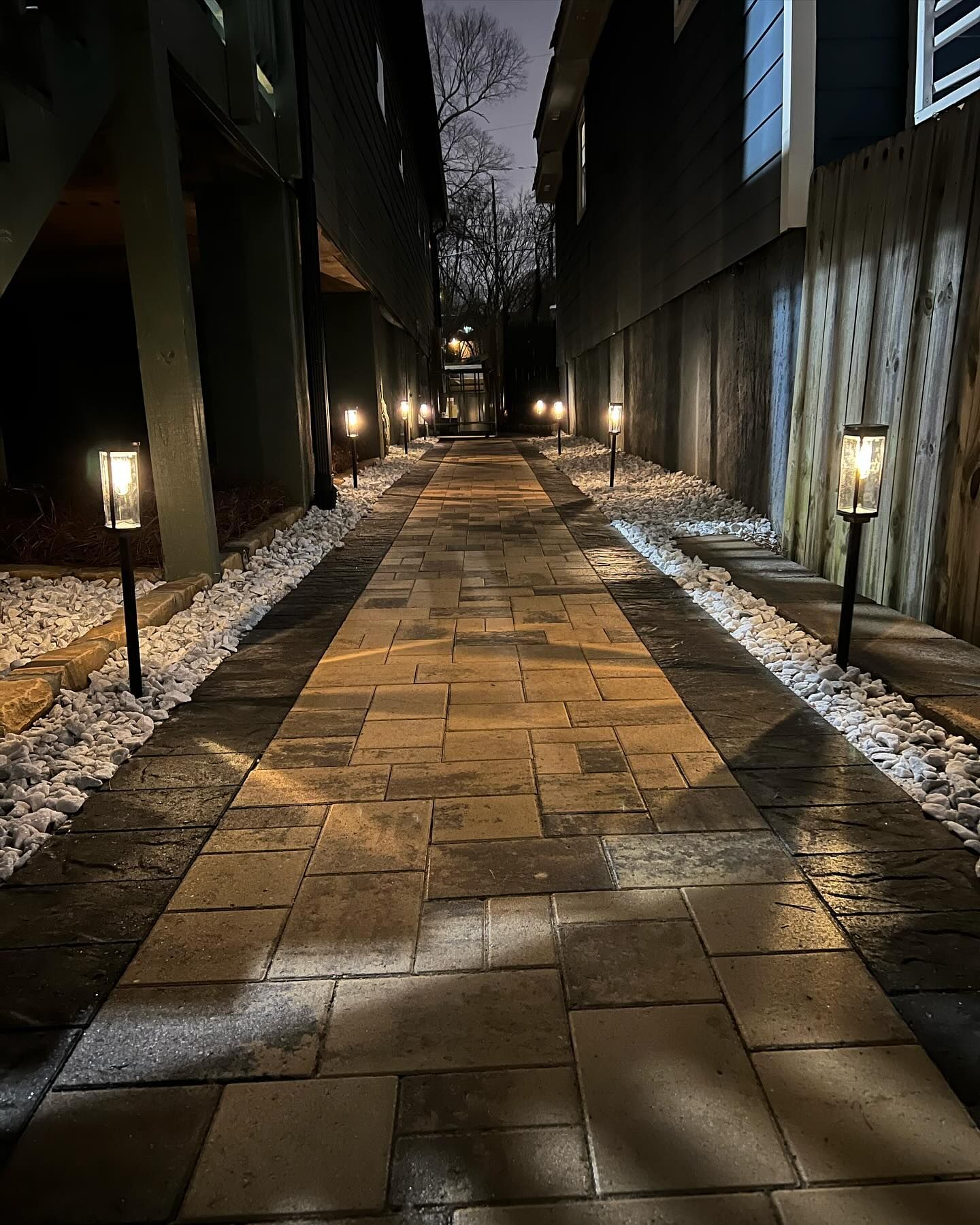 Narrow brick path illuminated by lights between two buildings at night.