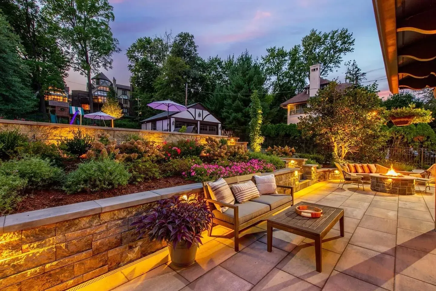 A patio with a couch , chairs , a table and a fire pit.