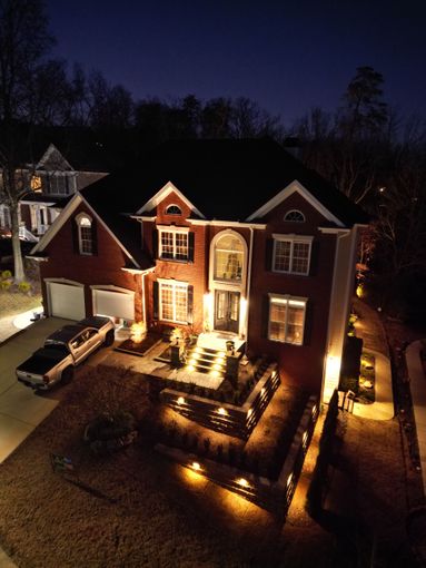 Night view of a brick house lit by outdoor lighting. A car sits in the driveway.
