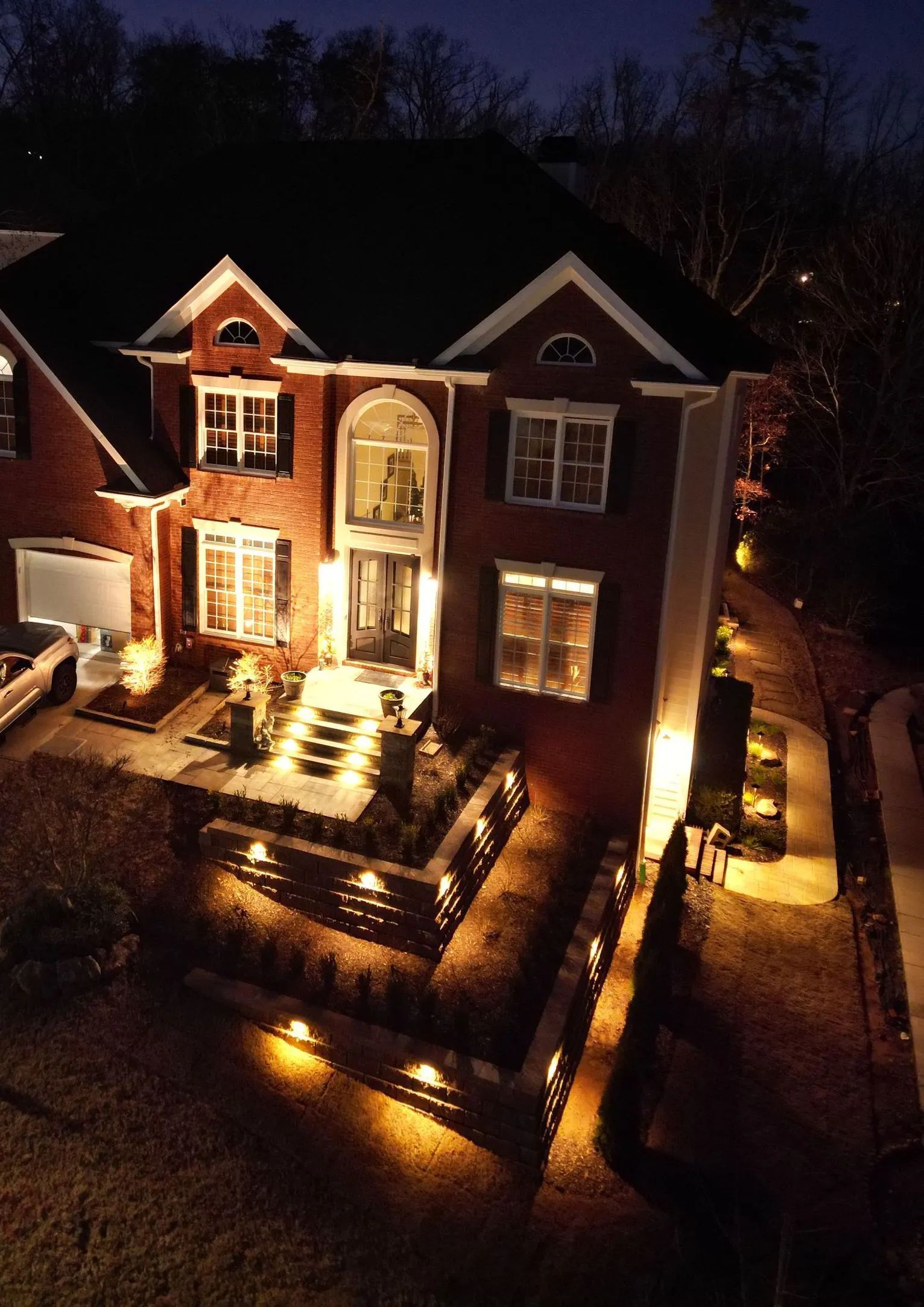 A well-lit, brick house at night with landscape lighting illuminating the front steps. 