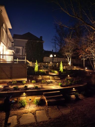 Nighttime outdoor garden with illuminated steps and landscaping; person on the left.