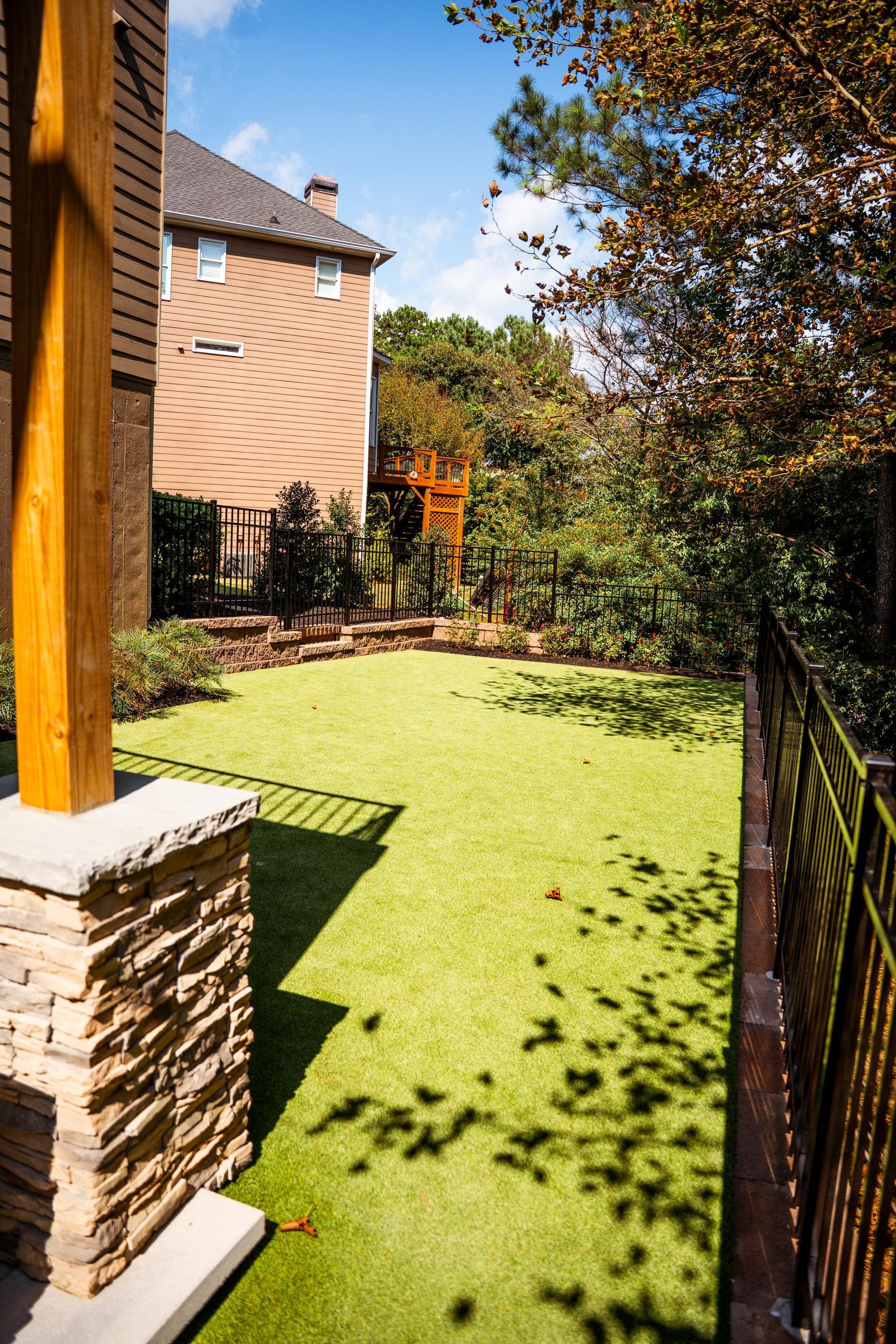 Green artificial lawn in a backyard, with a house on the left and trees along the back fence.