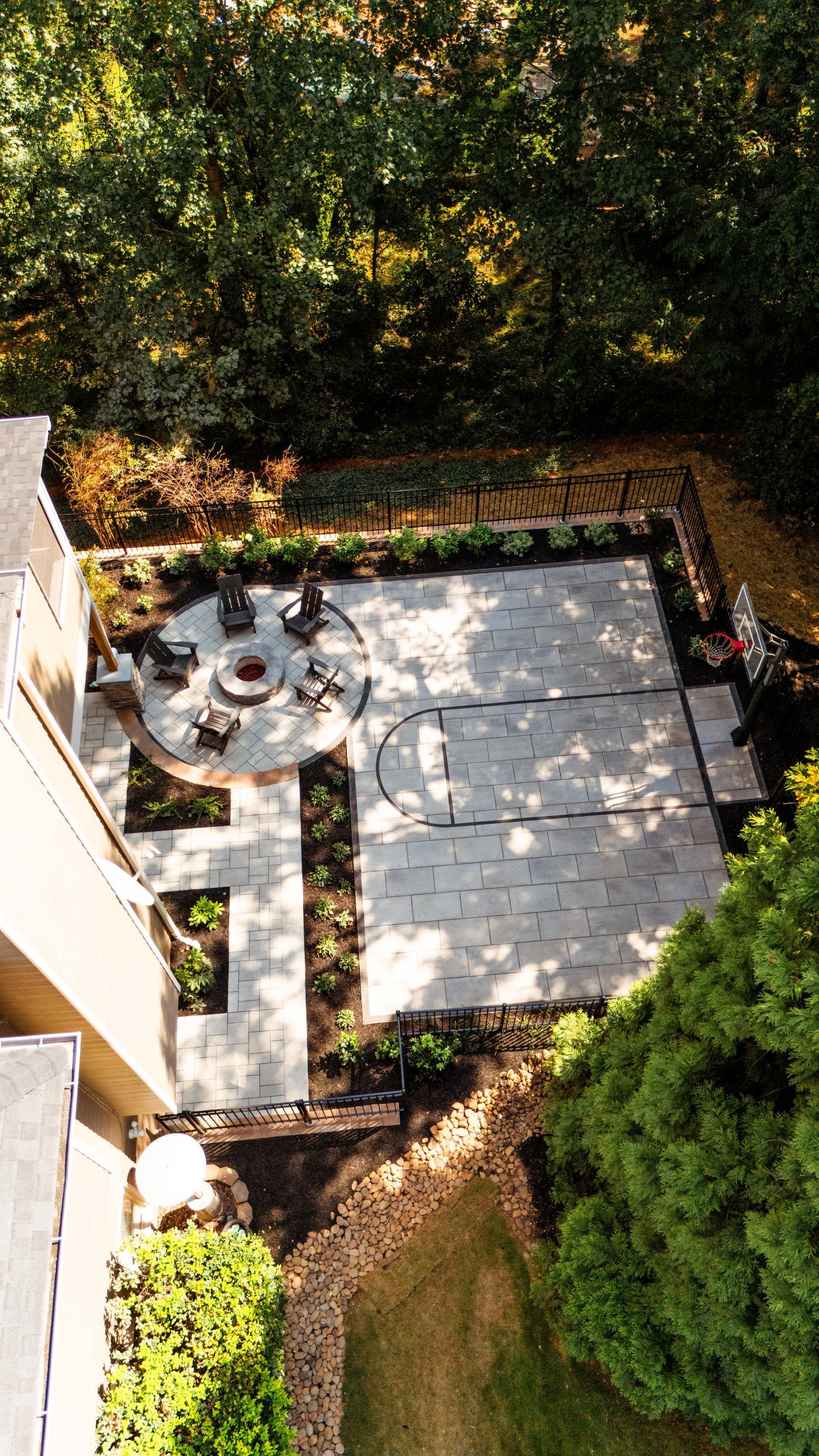Overhead view of a stone patio with a fire pit, seating, and surrounding landscaping.
