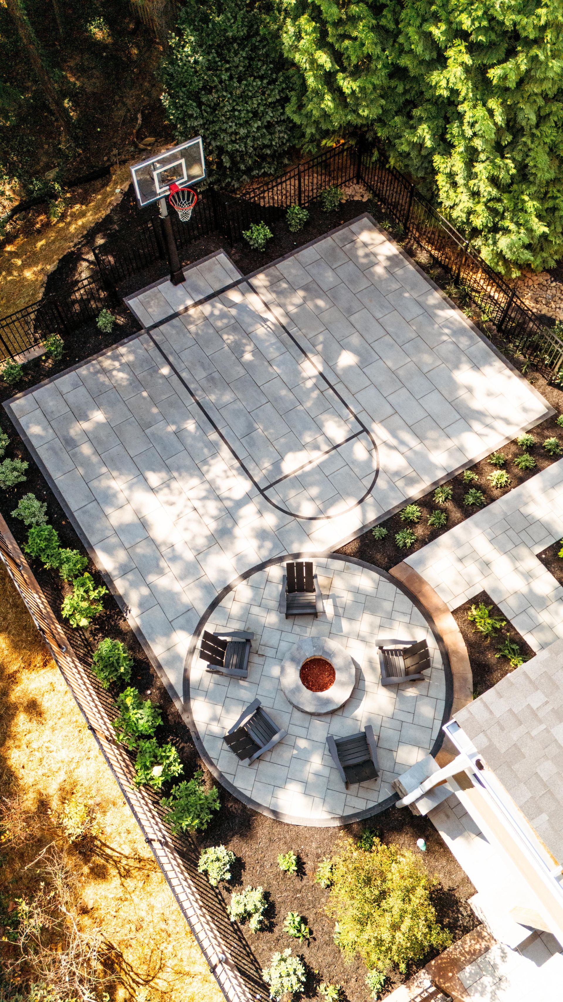 Overhead view of a backyard with a basketball court, fire pit with chairs, and landscaping.